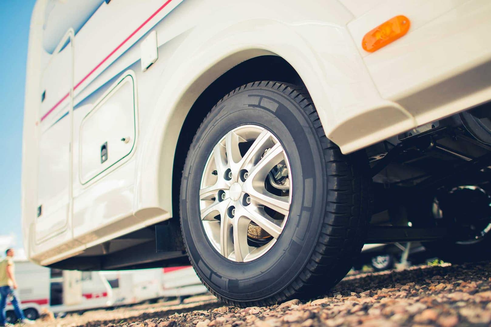 A white RV with a tire parked in a gravel lot, using a Run-Flat Device for RV Safety.