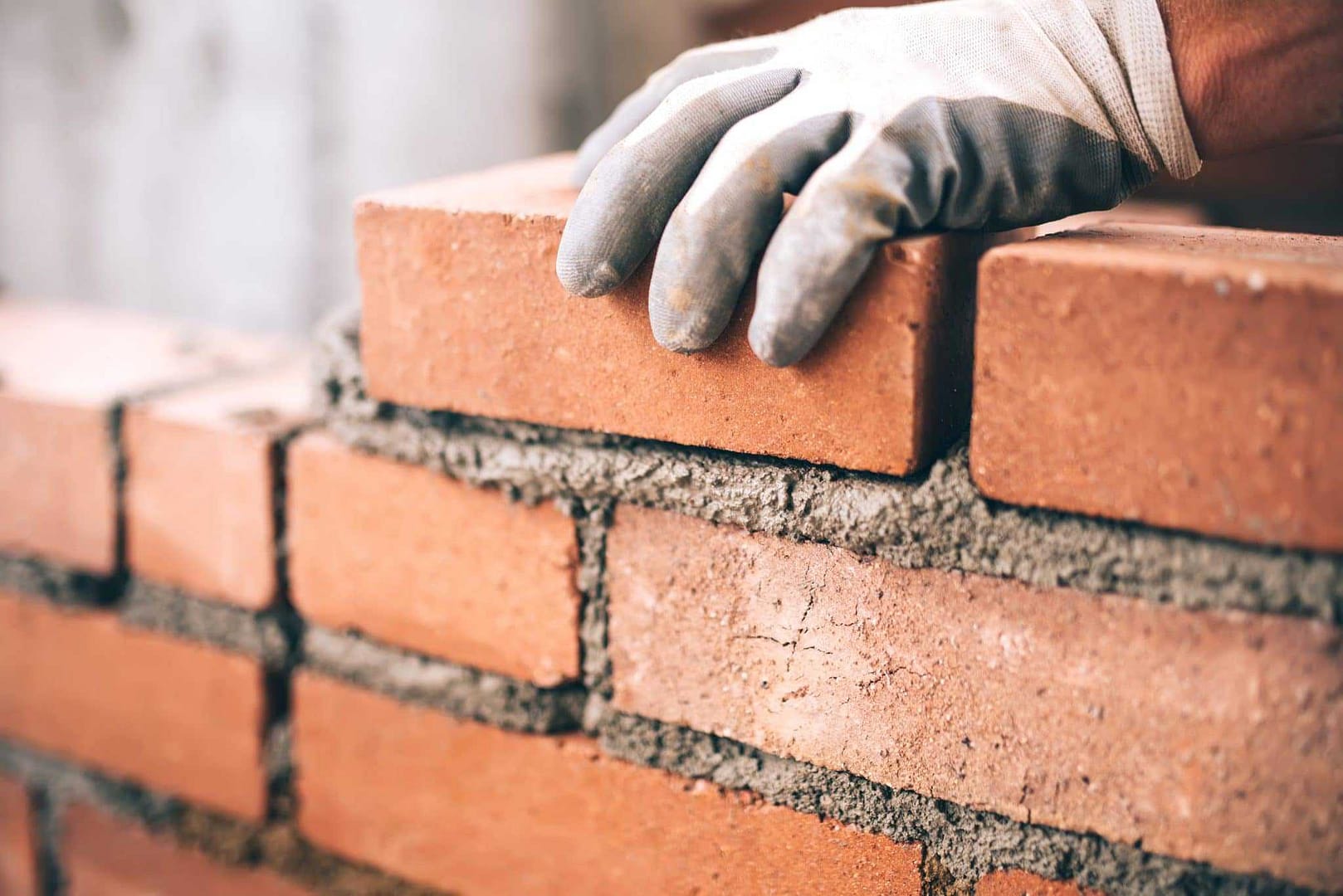 A person wearing gloves is working on a brick wall.