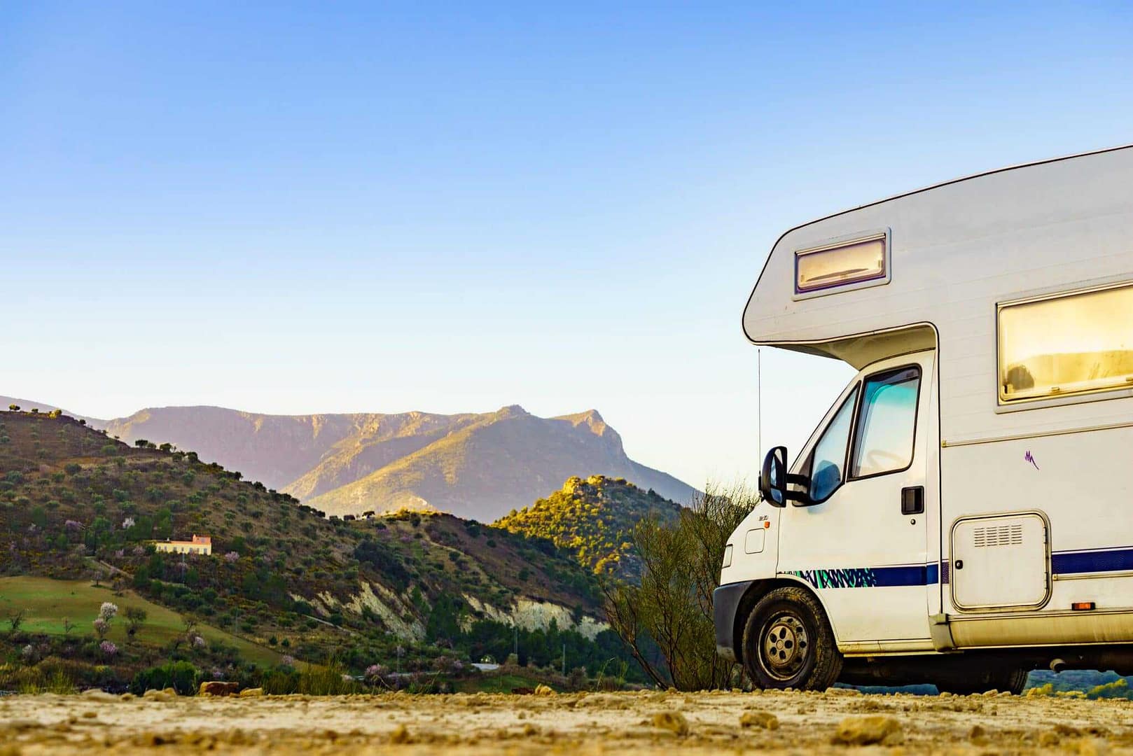 A white motorhome parked on a dirt road with mountains in the background.