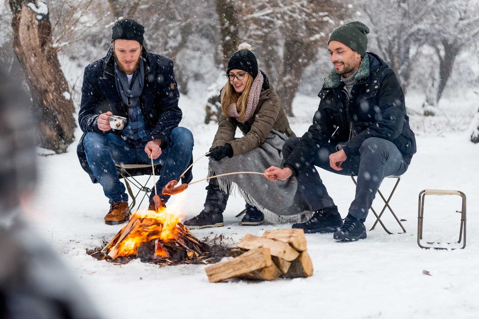 Winter camping at Jay Cooke State Park Campground, with a group of people sitting around a campfire in the snow.