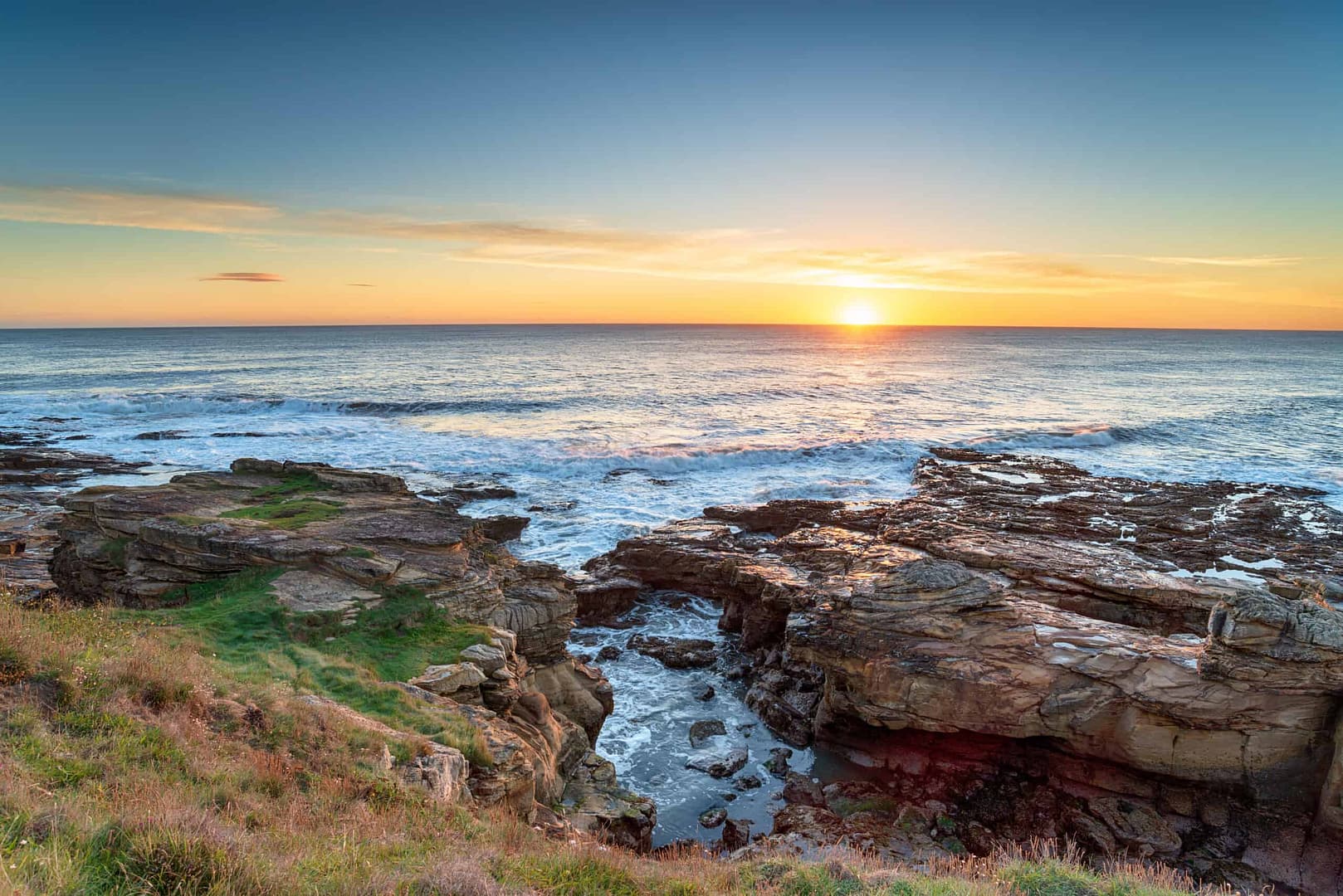 The sun is setting over Druridge Bay, a stunning location along the Northumberland Coast, surrounded by rocky cliffs. Nearby, there is a tranquil campsite where you can fully immerse