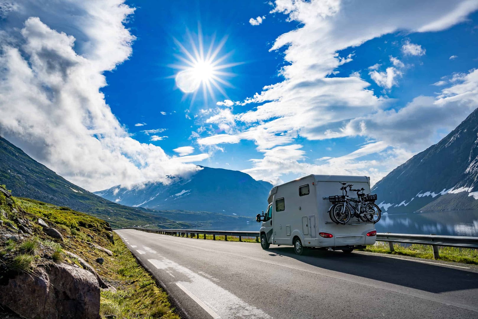A Roamly-branded rv is driving down a road with mountains in the background.