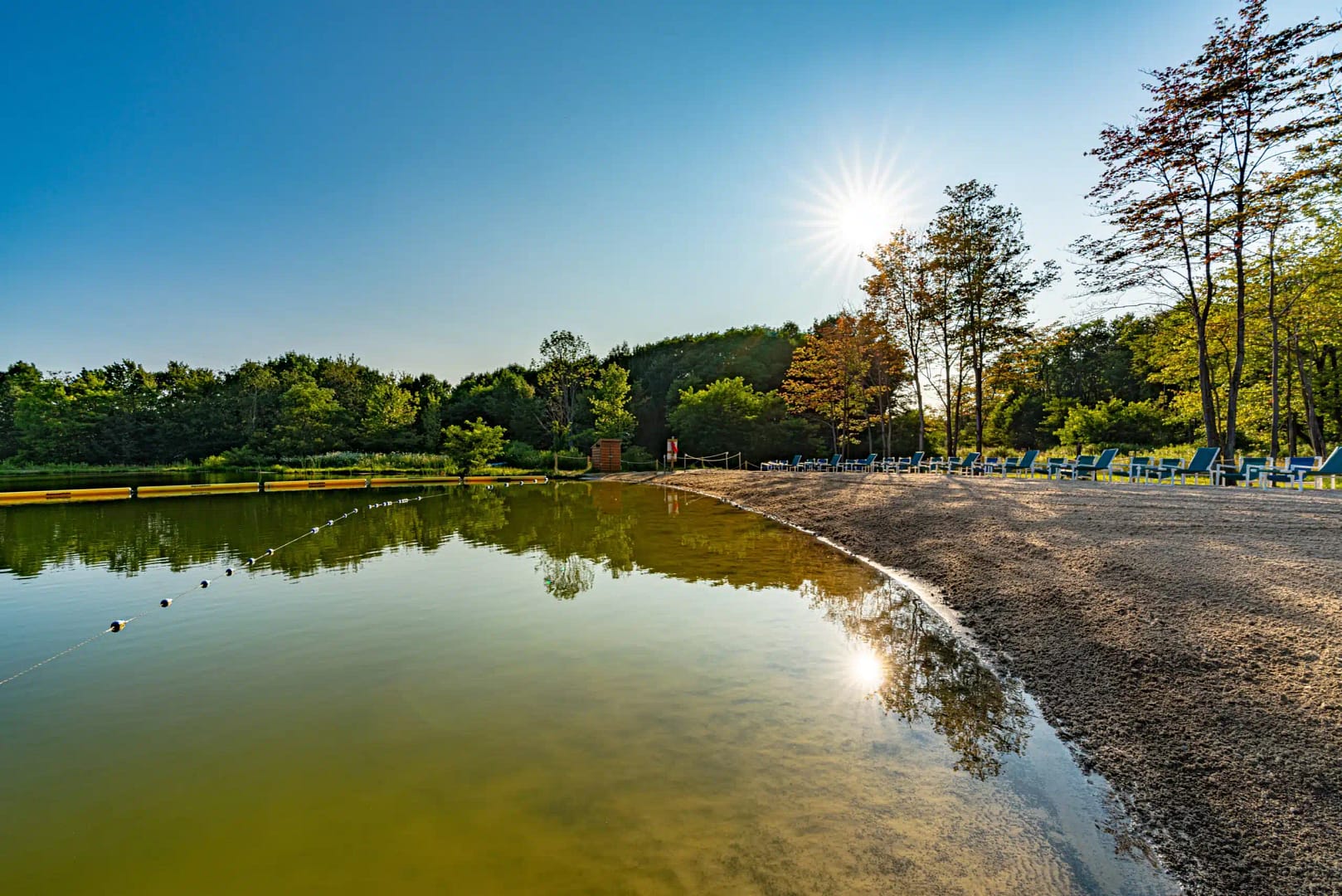 IHM Outdoors presents a serene pond with trees and a sun shining on it.