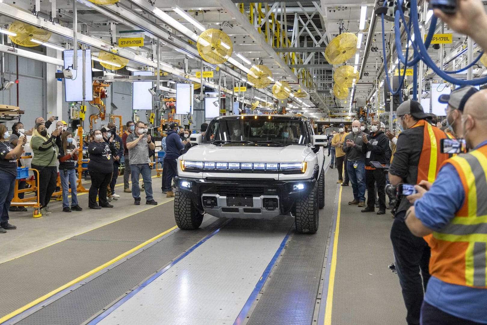 A group of people are taking pictures of a General Motors off-road supertruck in a factory.