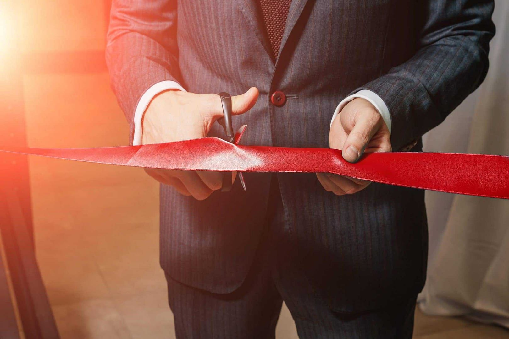A man in a suit cutting a red ribbon.