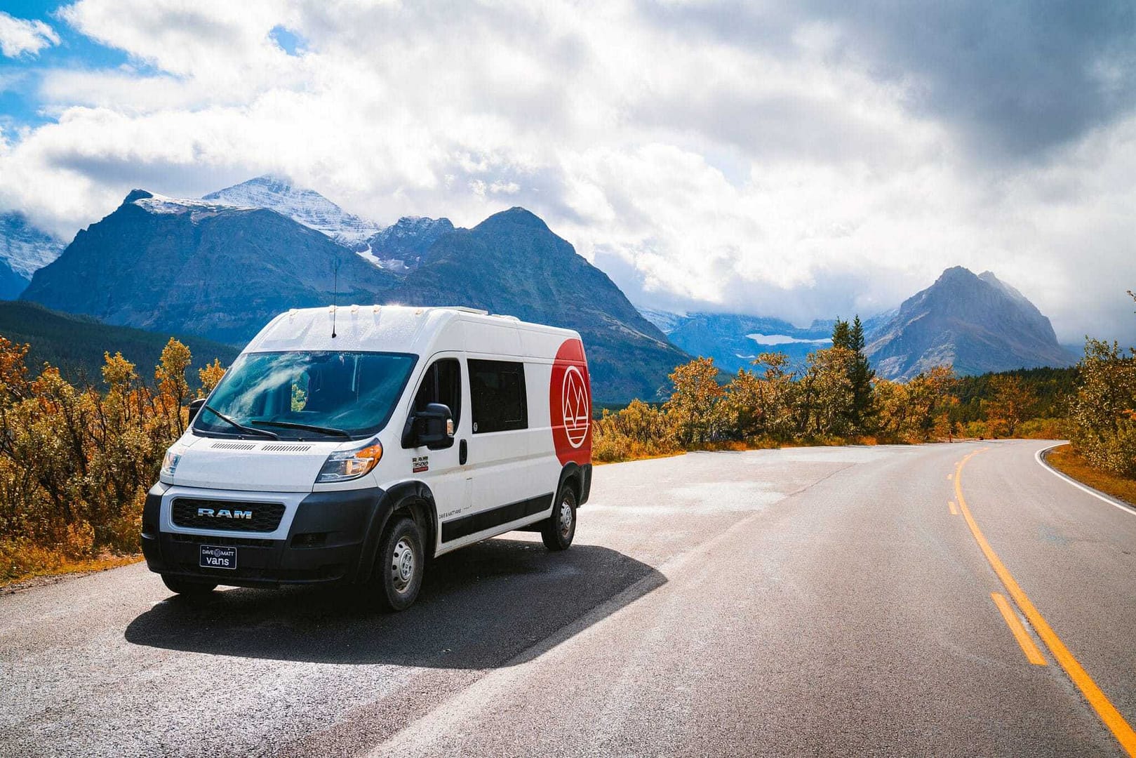 A white van from Dave & Matt Vans accelerates down a road with mountains in the background.