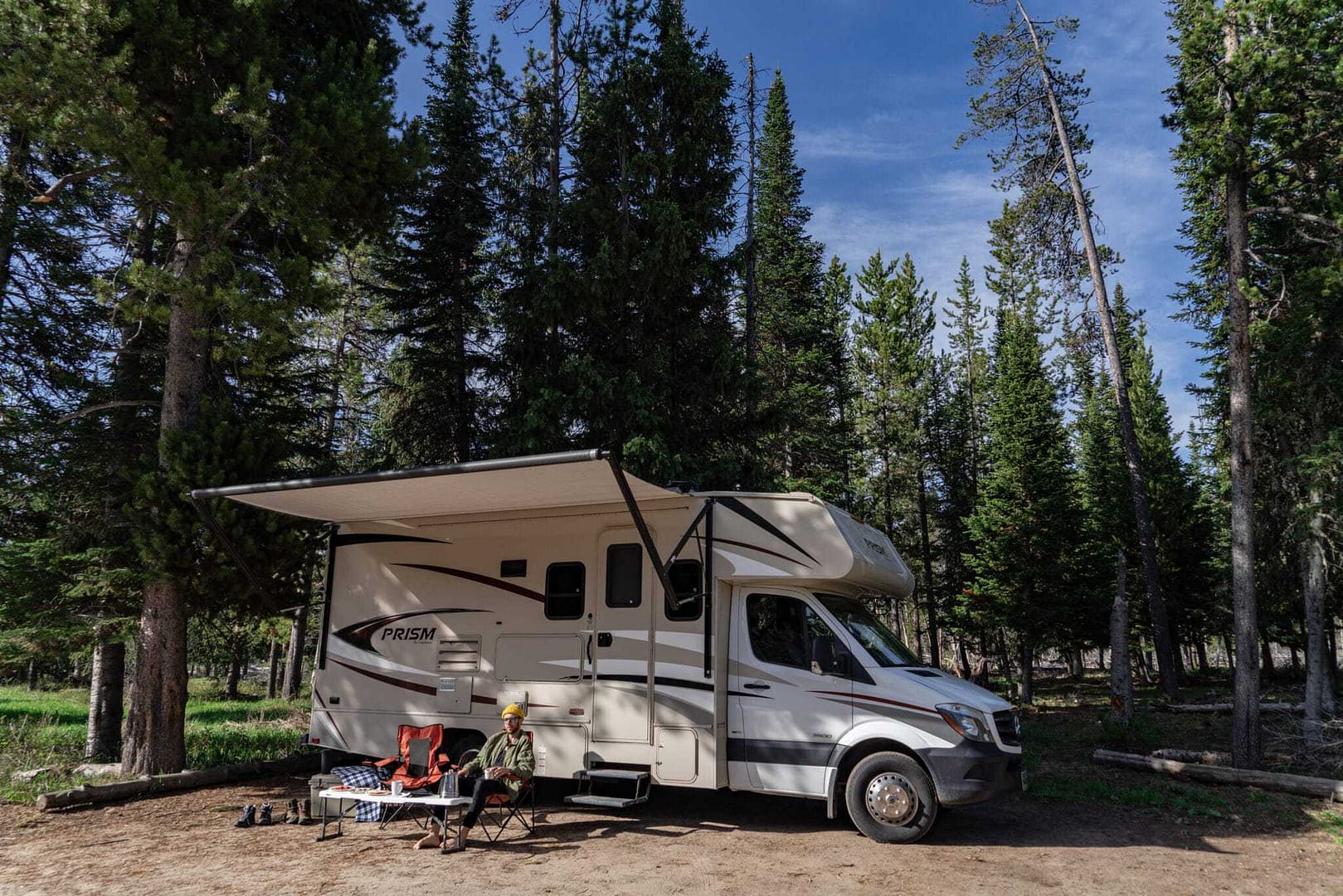 An RV parked at a campground in a forest near trees, offering a networking opportunity for RVshare users.