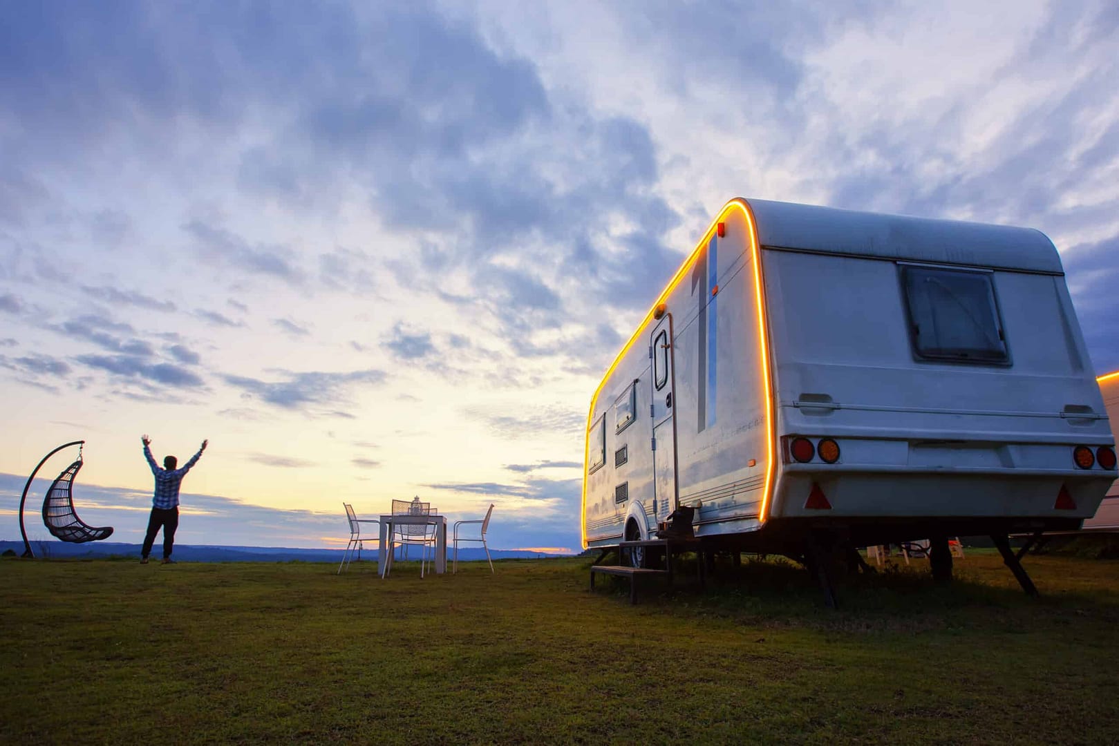An Australian is standing in front of a caravan at sunset, contributing to the Boost Economy in the Caravan Industry.