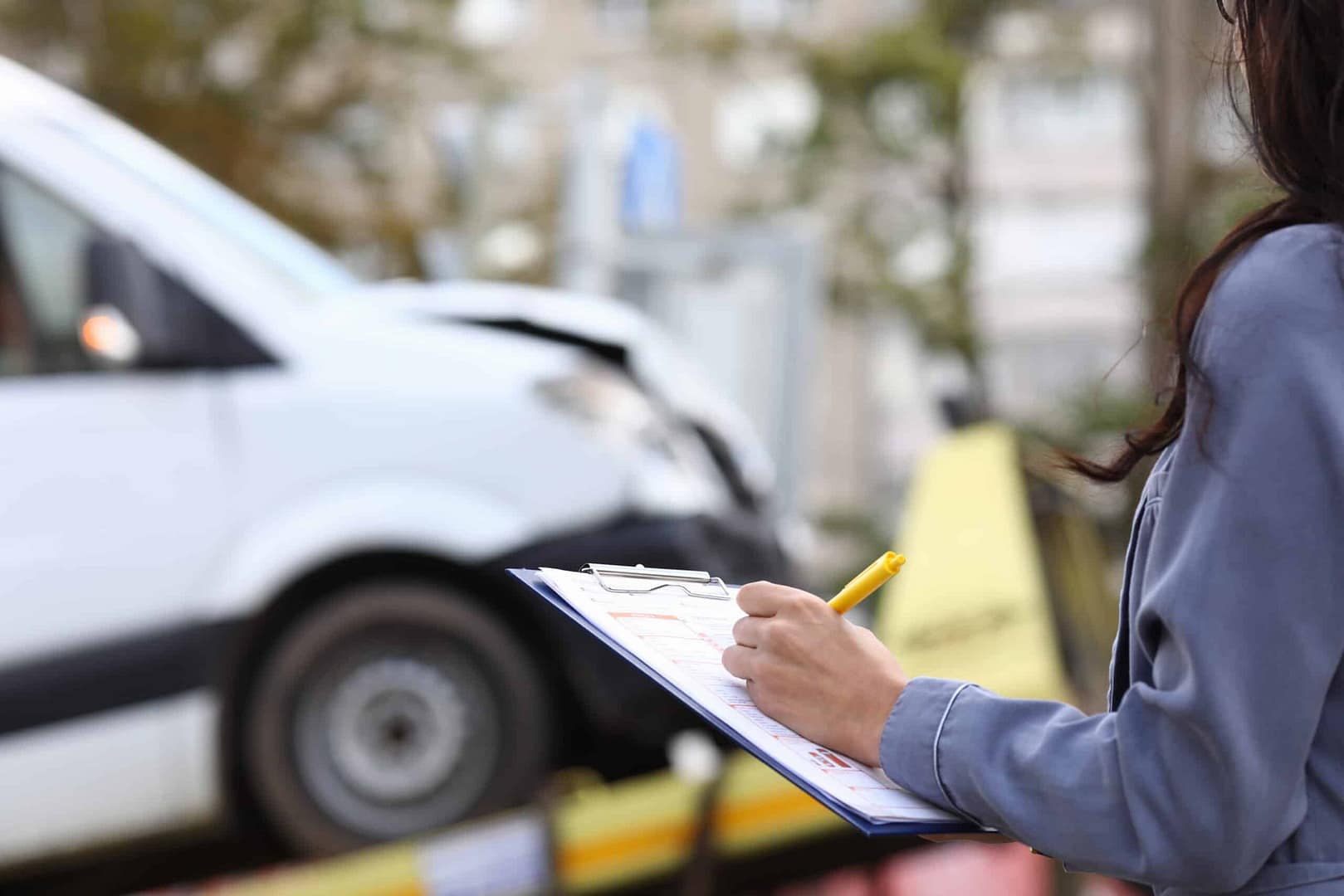 A woman writing on a clipboard in front of an AIB Australia van, reviewing the Outdoor Liability Insurance Package.