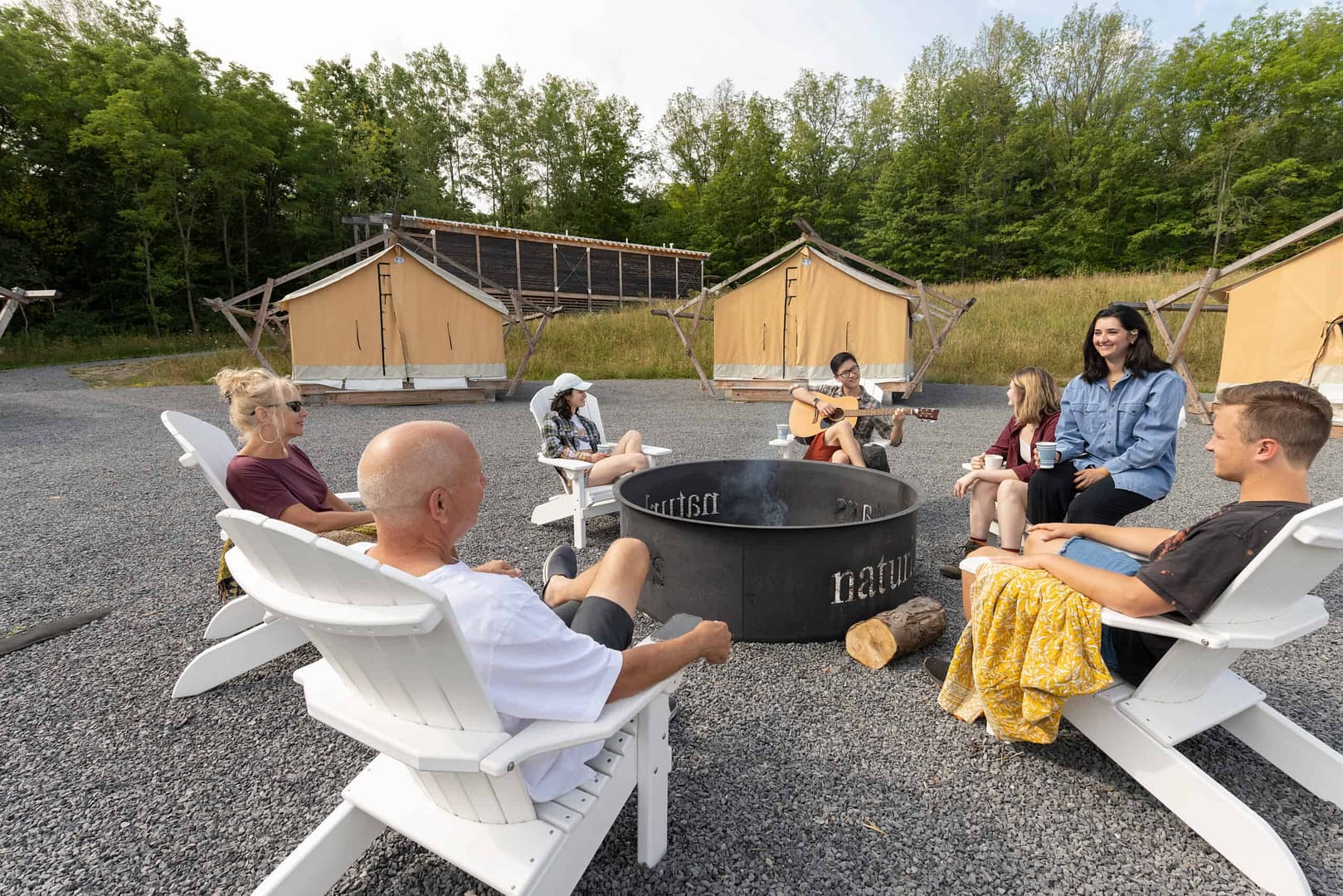 A group of people sitting around a fire pit under a starry night sky in front of Naturluxe tents.