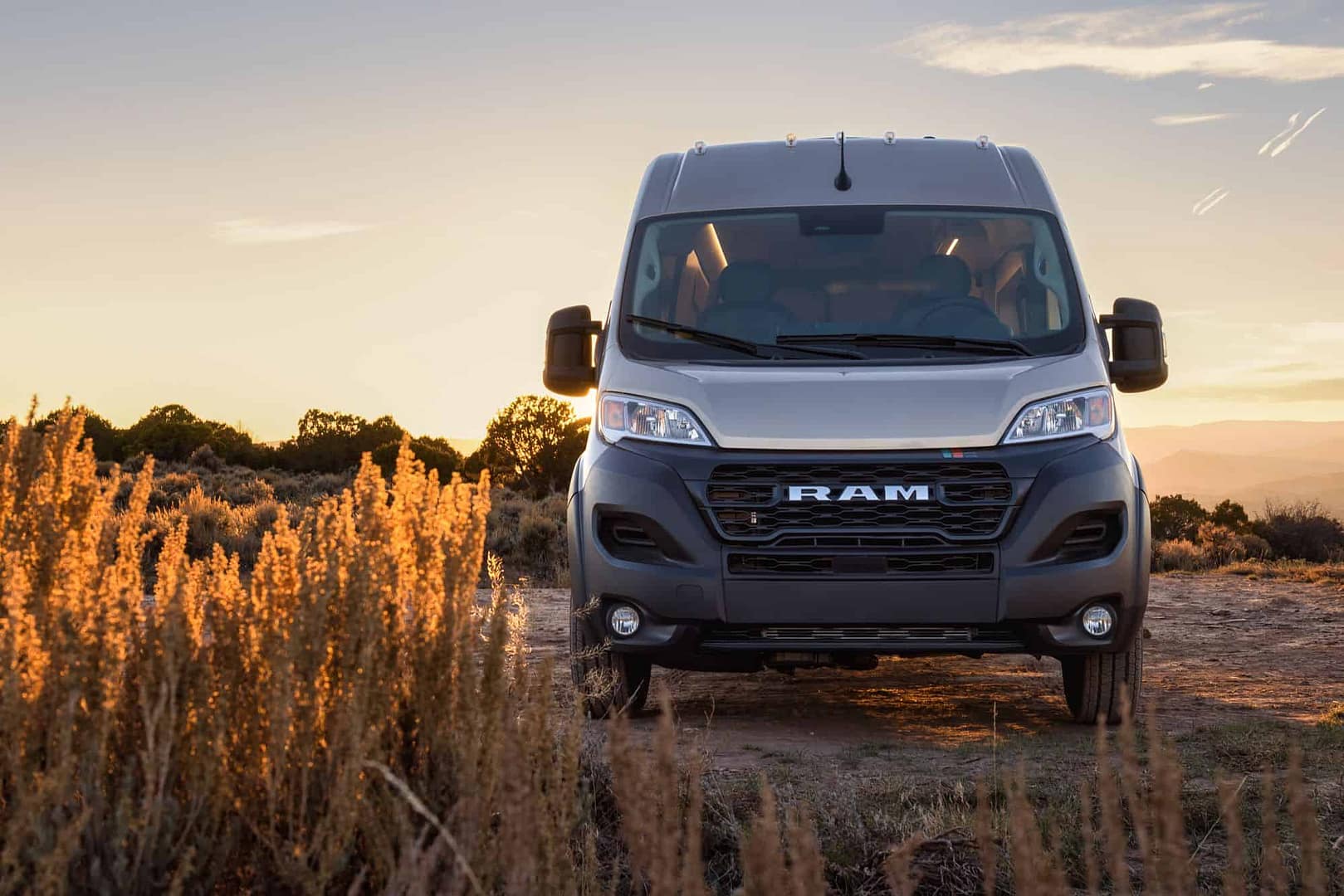 A silver van from Dave & Matt Vans is parked on a dirt road at sunset.
