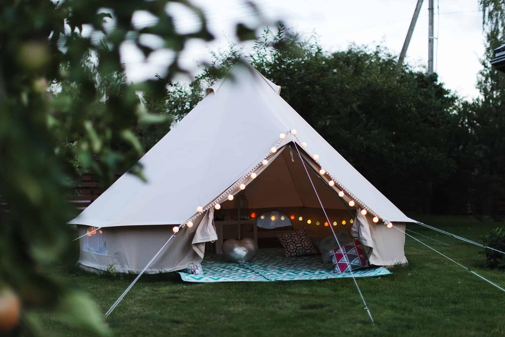 A luxurious white teepee tent is set up in a backyard, providing a Timberline Glamping experience.