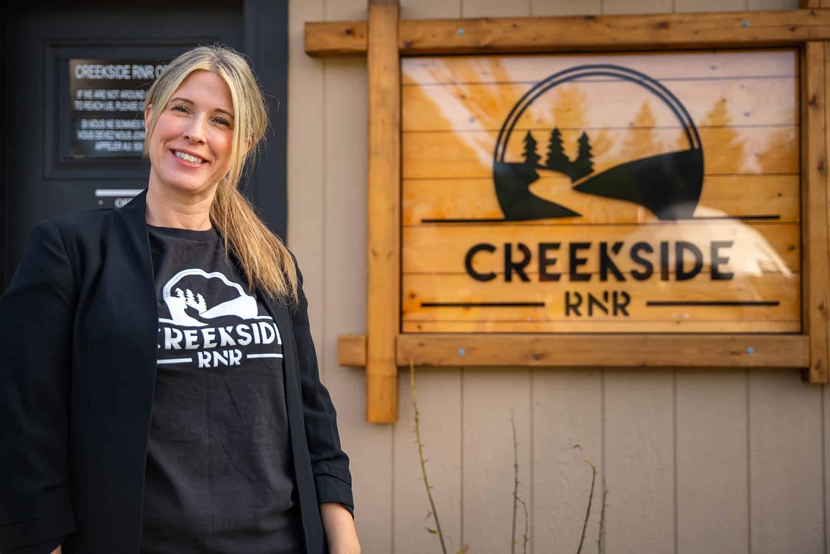 A visionary woman standing confidently in front of a sign that says Creekside Inn, exemplifying the victory of her entrepreneurial pursuits.