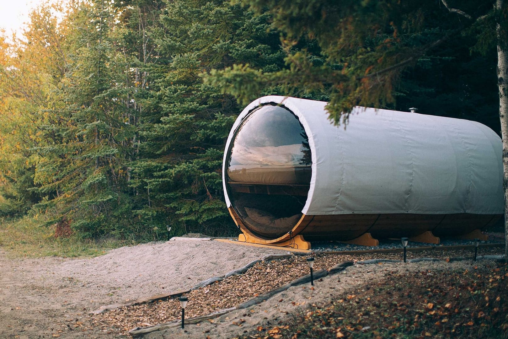 A round tent in the woods next to a tree, nestled in a Canadian Sleeping Barrel at a campground or RV park.