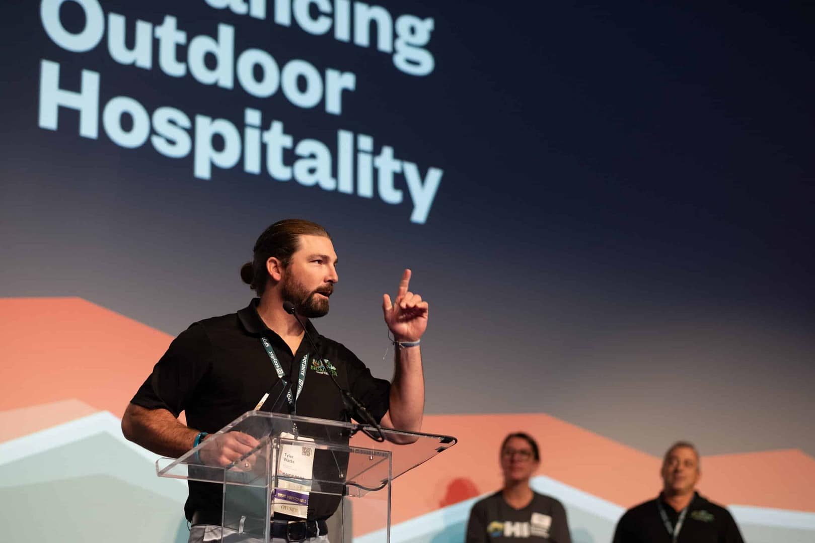 A man giving a speech at the OHCE2023, an outdoor hospitality event celebrating excellence and presenting Awards of Excellence.