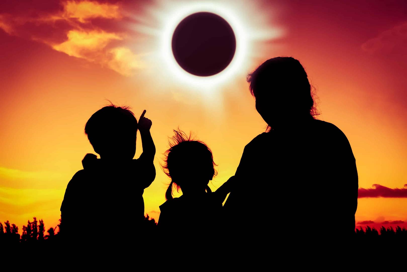 Silhouetted family at a campspot watching a solar eclipse at sunset, with one child pointing upwards at the darkened sun.