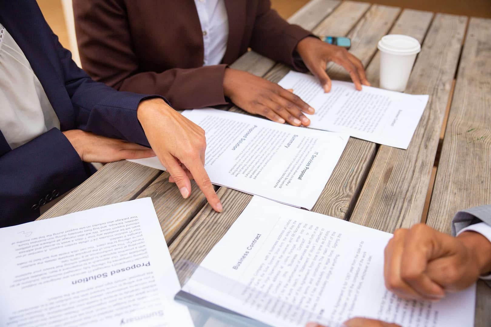 Four people in business attire sitting around a wooden table, discussing and pointing to documents about the recent resident backlash at Grandview RV Park, with a coffee cup and smartphone visible on the table.