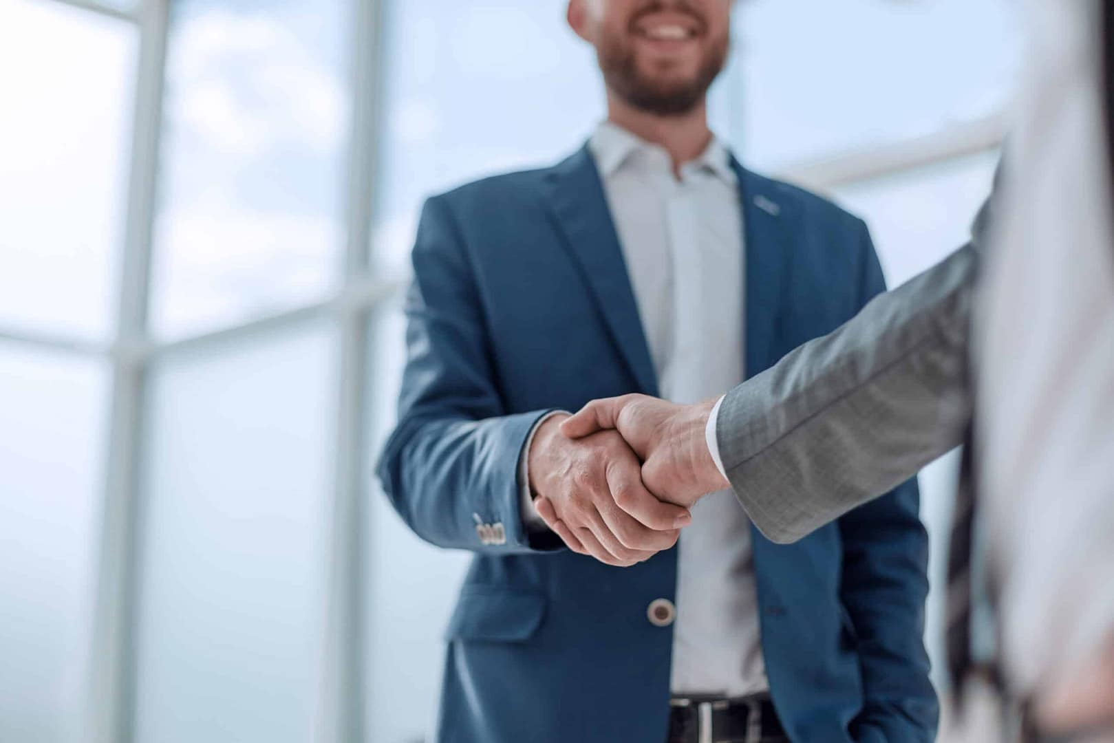 Two individuals in business attire shaking hands in a bright indoor setting, signaling agreement or partnership, possibly regarding an insurance deal for adventurous Canadians.