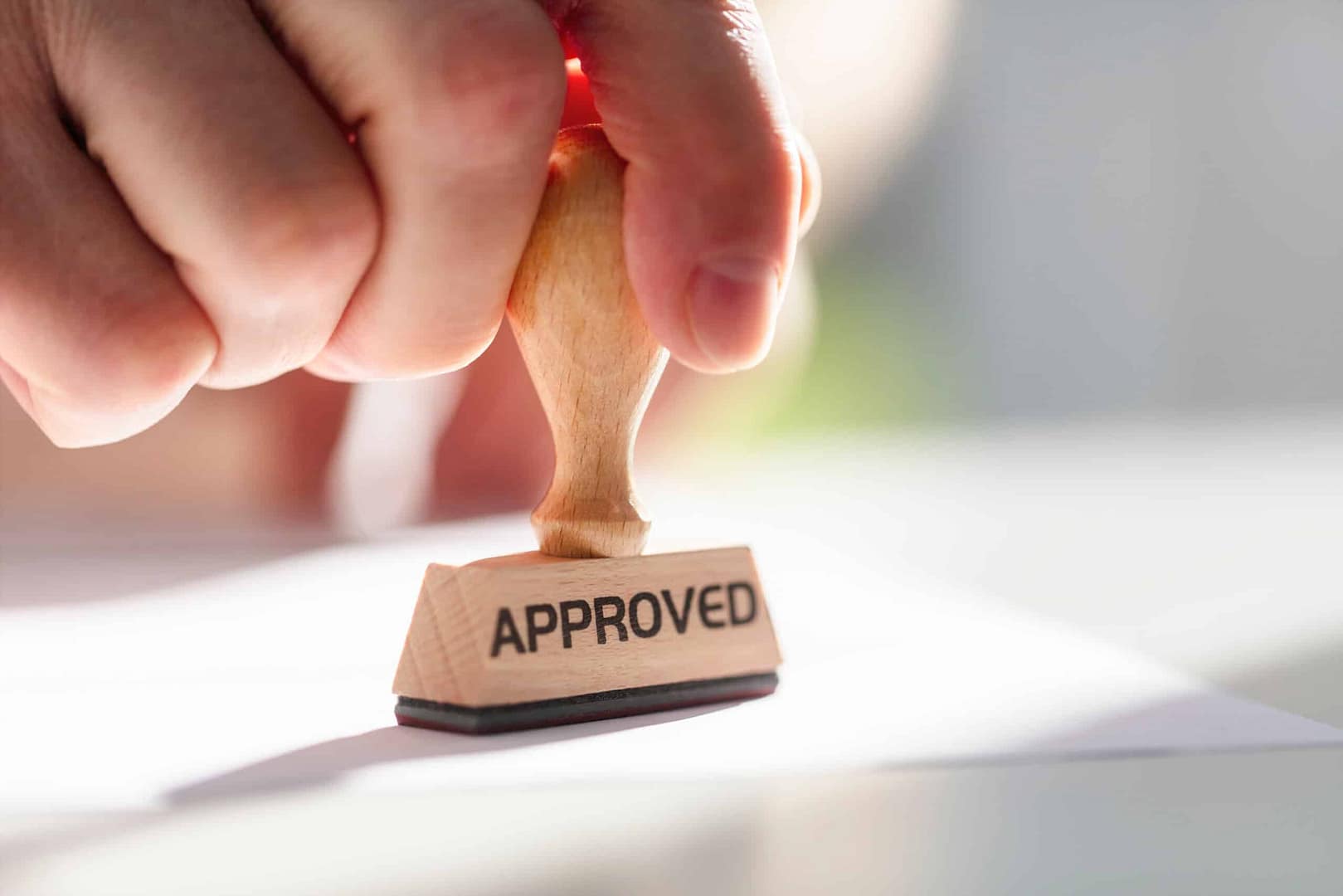 A hand pressing a wooden stamp marked "Auto Draft" onto a document, backlit by bright light.