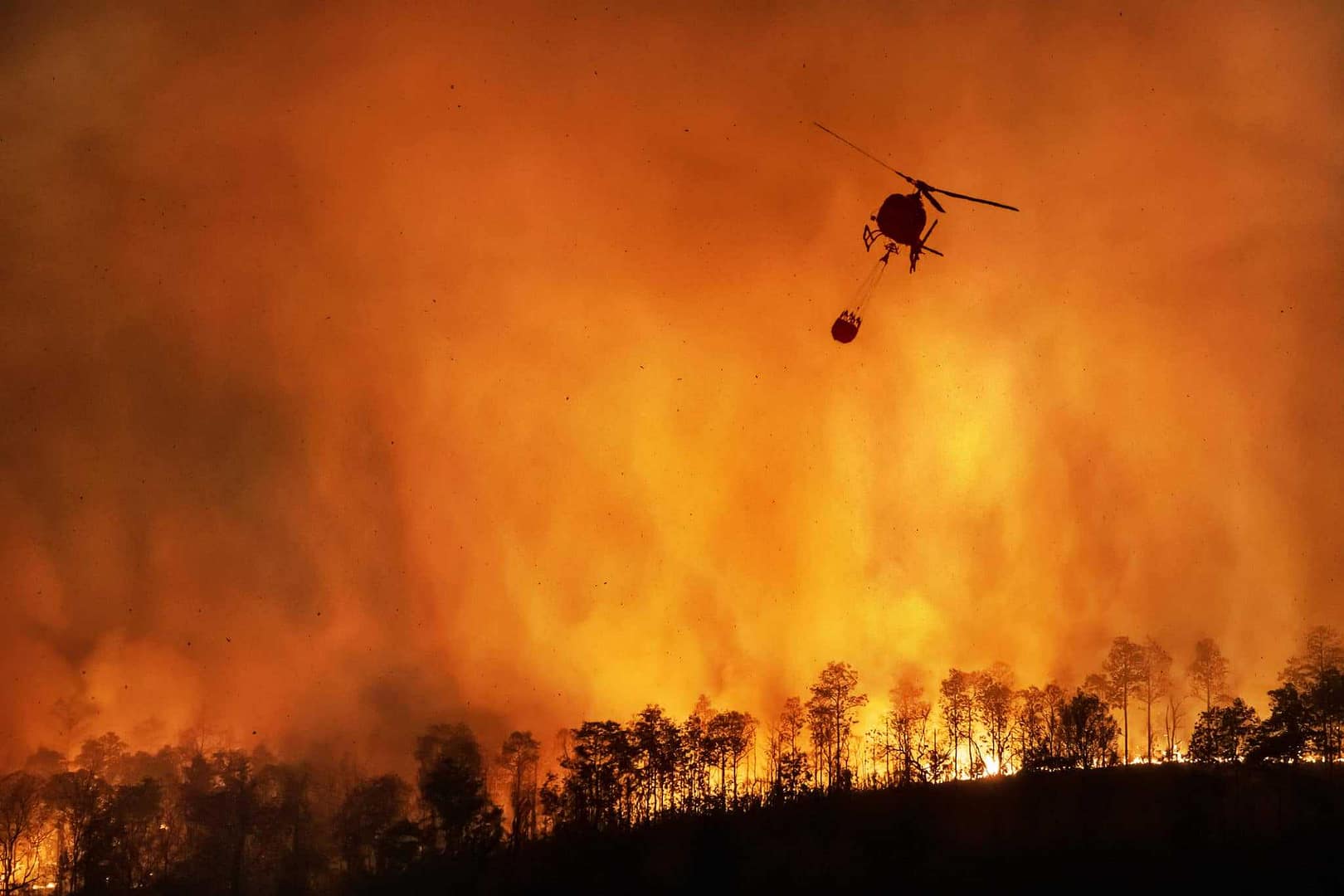 A helicopter flies toward the Tahoe Basin, observing the Caldor Fire raging through the forest.