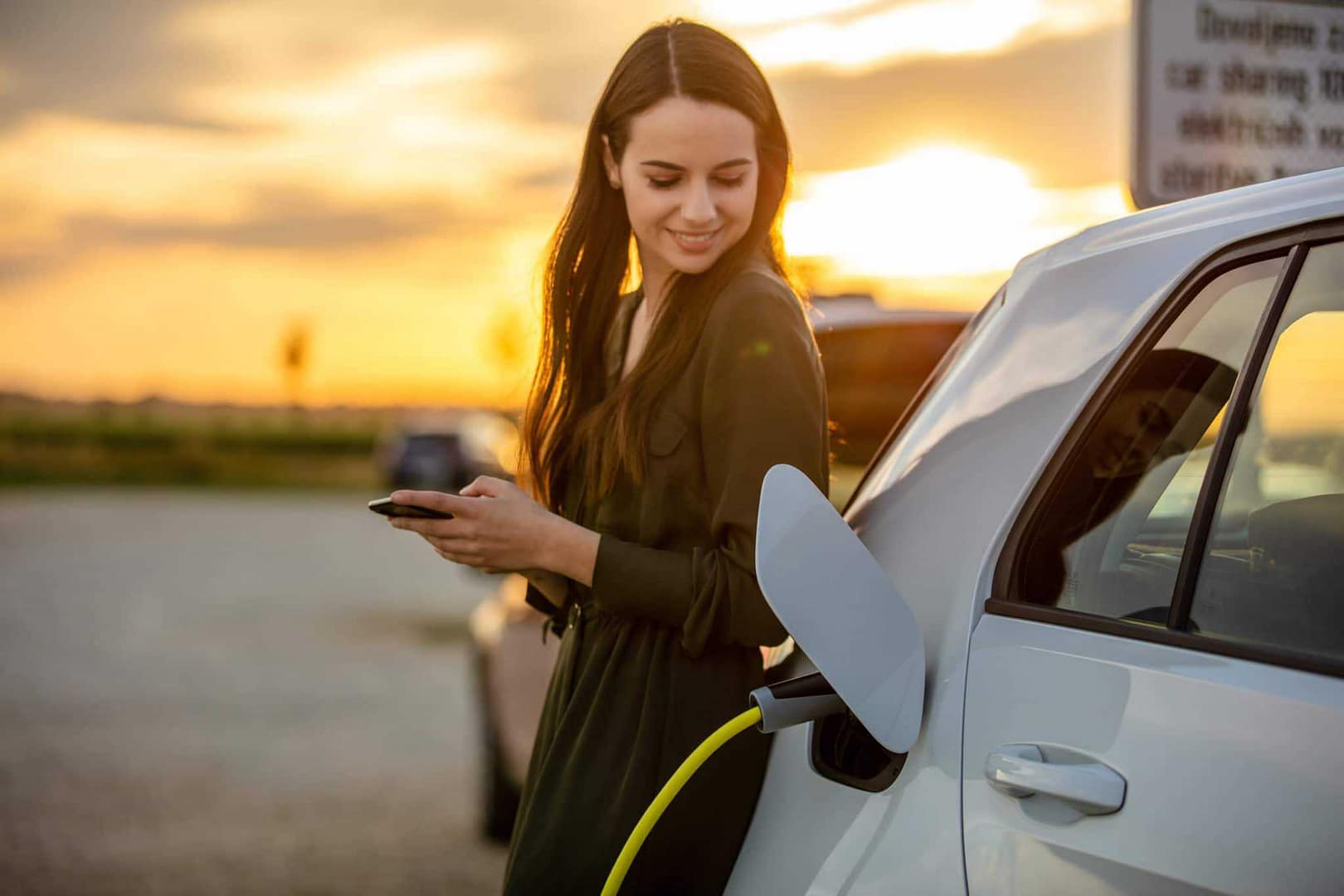A woman charging her electric vehicle while looking at her phone.