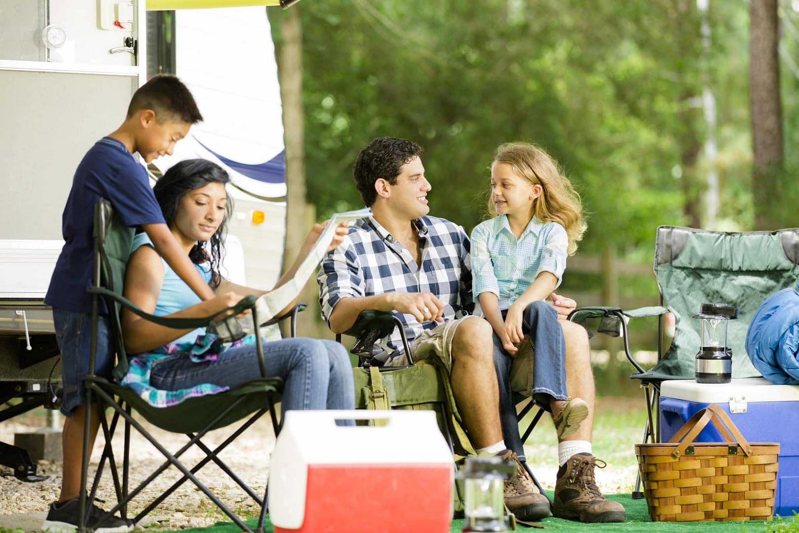 A young family sits in front of an RV and reads a book, envisioning their future adventures as proud owners.