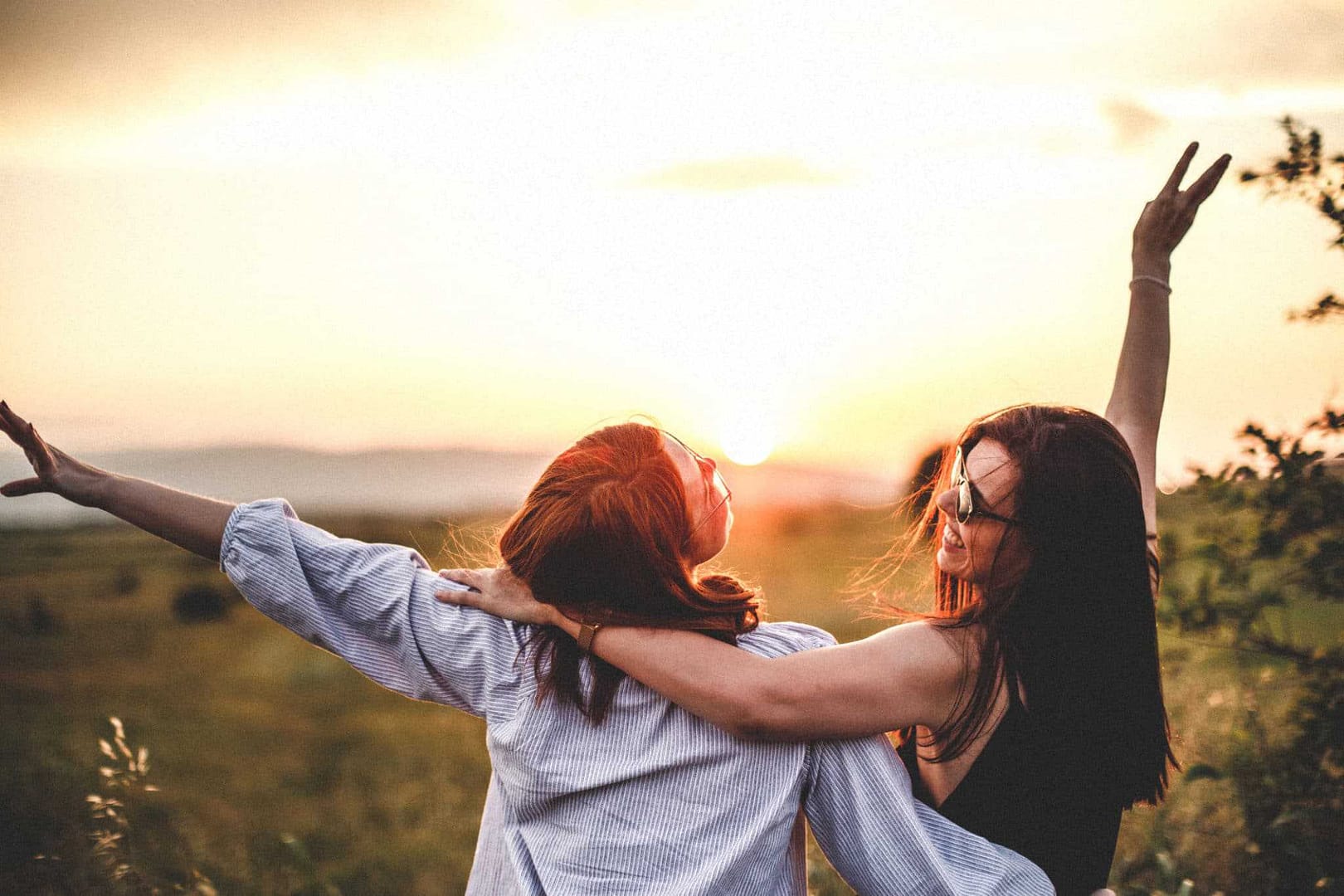 Two women standing in a field at sunset, enjoying luxury glamping in a train carriage amidst the beautiful landscape of New Zealand.