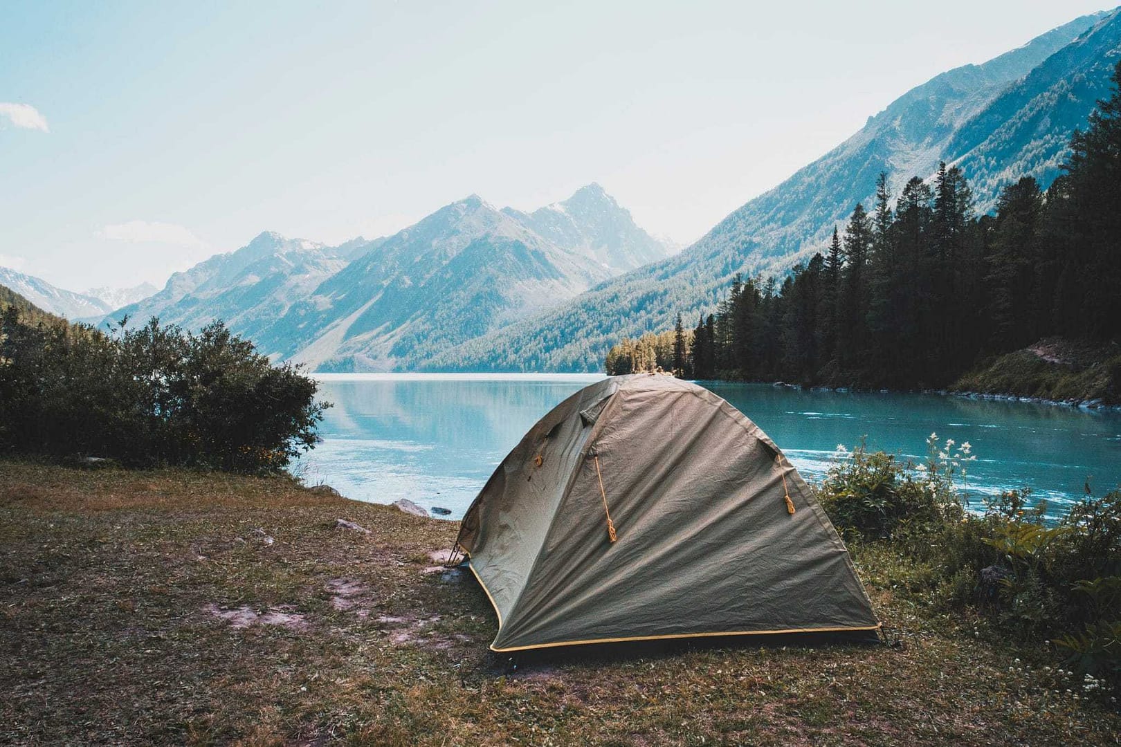A Regular Campers' tent pitched in front of a lake with mountains in the background.