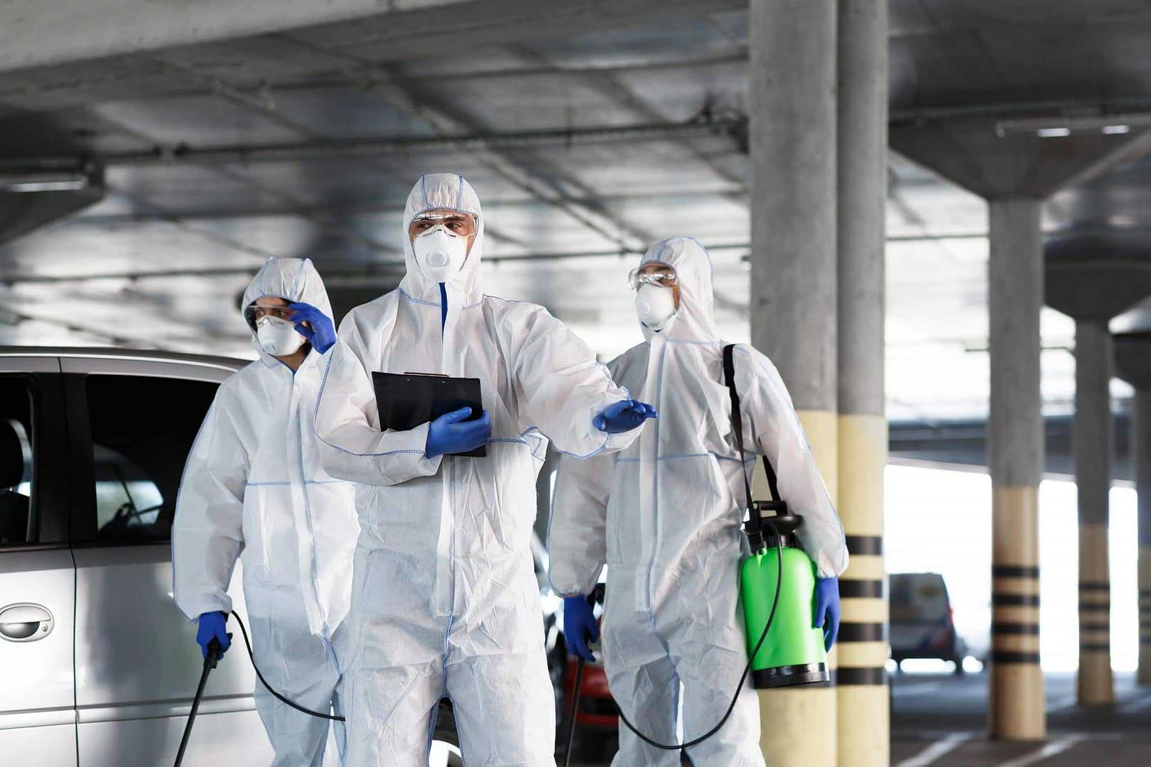 Three Tourism Operators in protective suits standing next to a car in a parking lot.