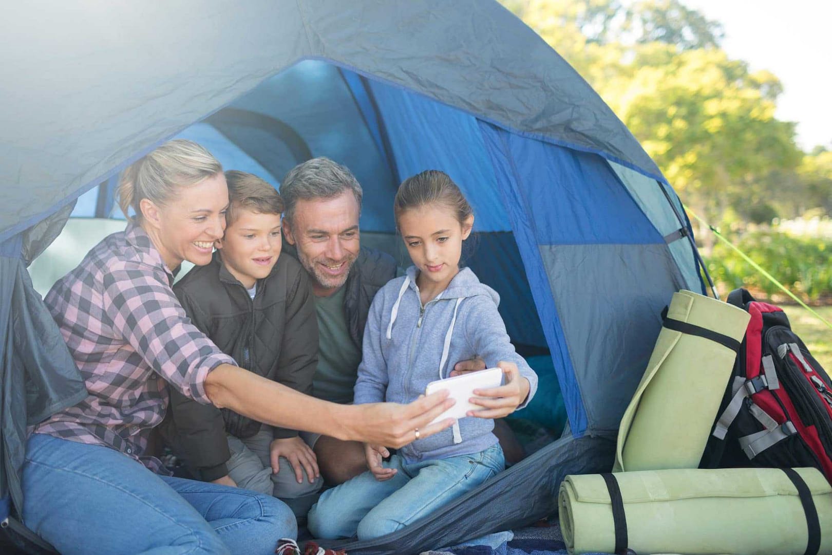 A family is sitting in a tent at a campsite, with a cell phone.