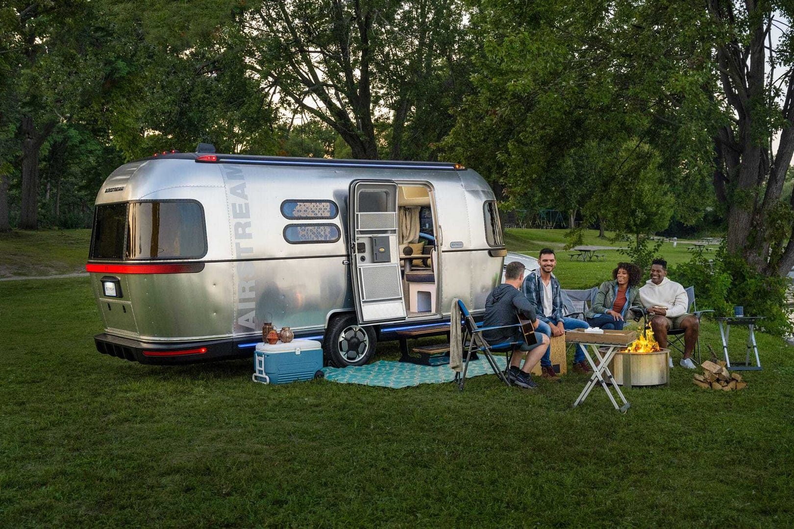 A group of people sitting around a THOR camper in the grass, exploring the world of electric RVs.