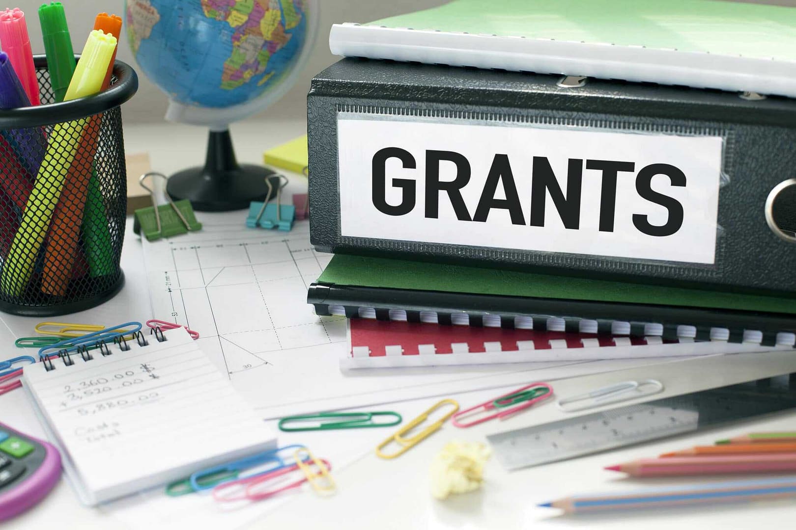 A binder with the word grants on it sitting on a desk.