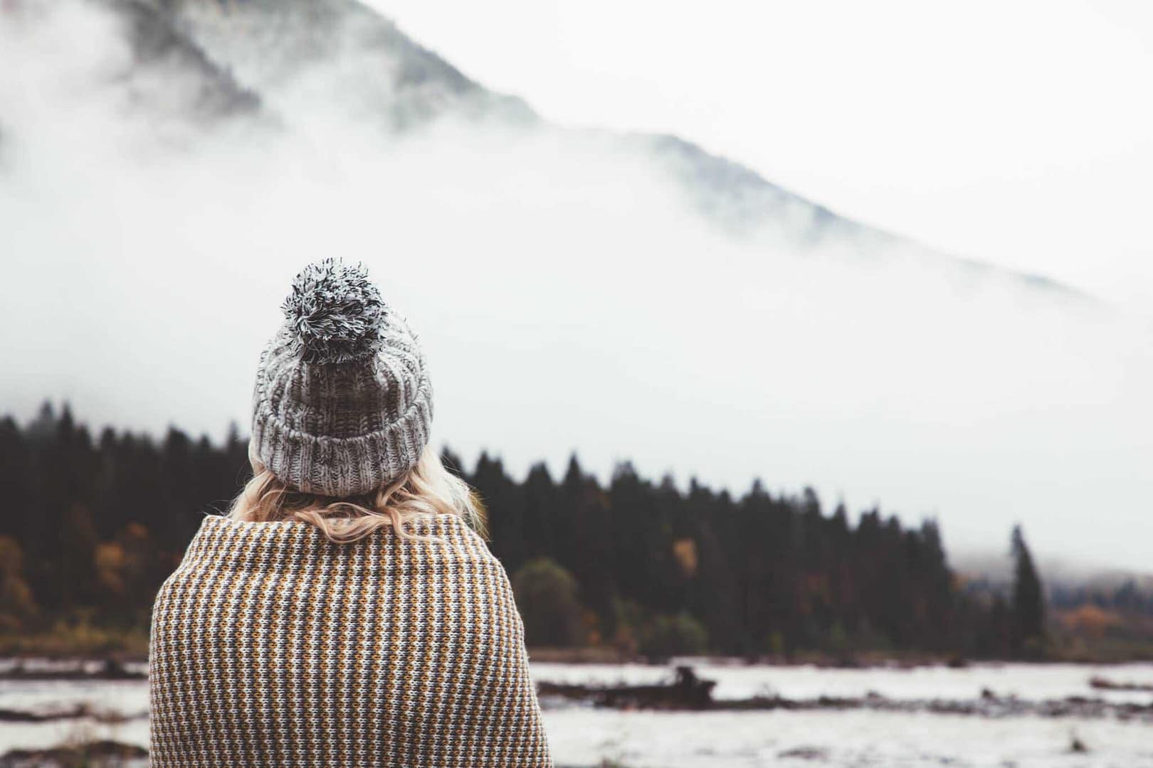 A woman wearing a beanie enjoying some time outdoors, looking out over a lake.