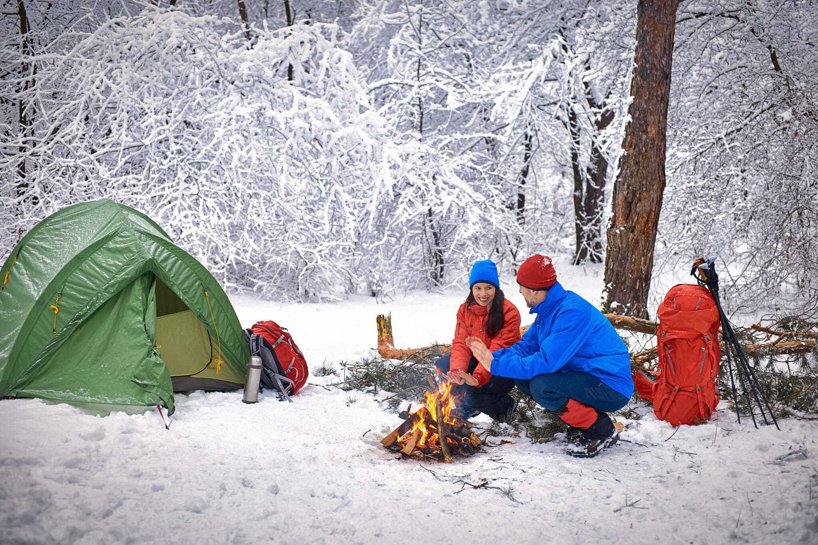 Two people sitting around a campfire in the snow.