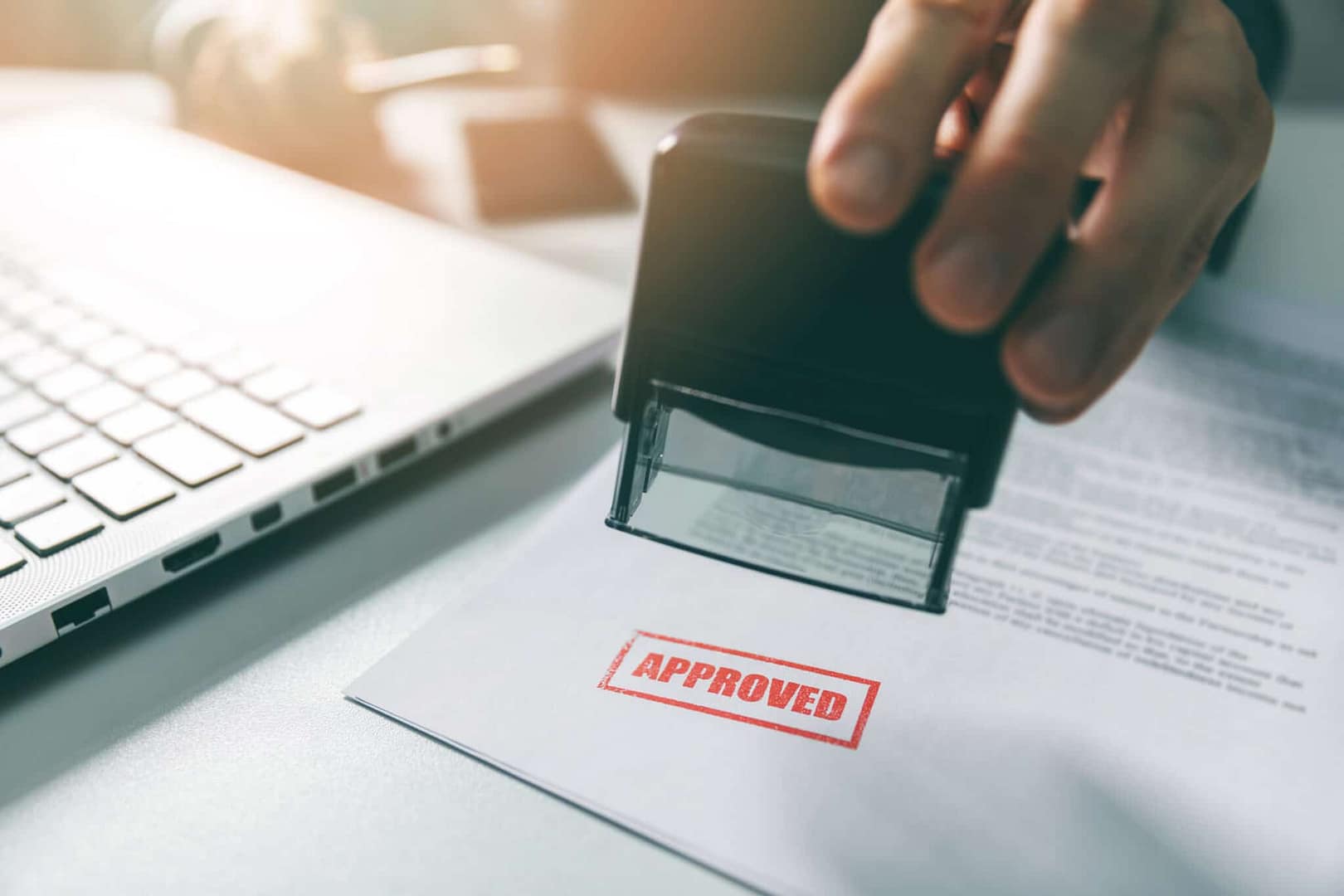 A person is stamping the word approved on a piece of paper.