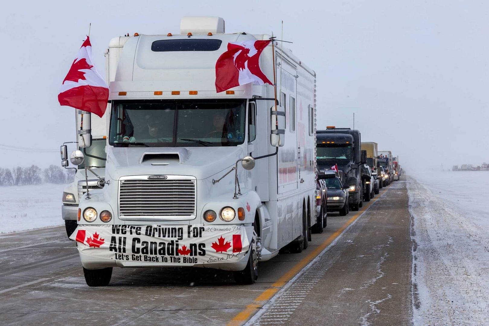 A group of trucks with Canadian flags on the road amidst truck blockades and a state of emergency.