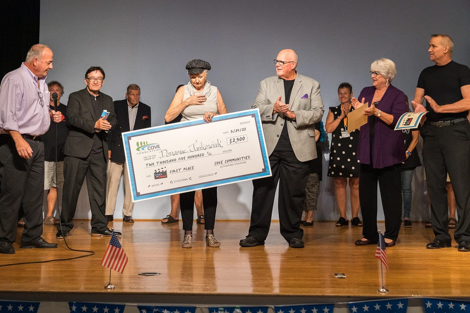 A group of people from Cove Communities, including Disabled American Veterans, raises a large check on stage.