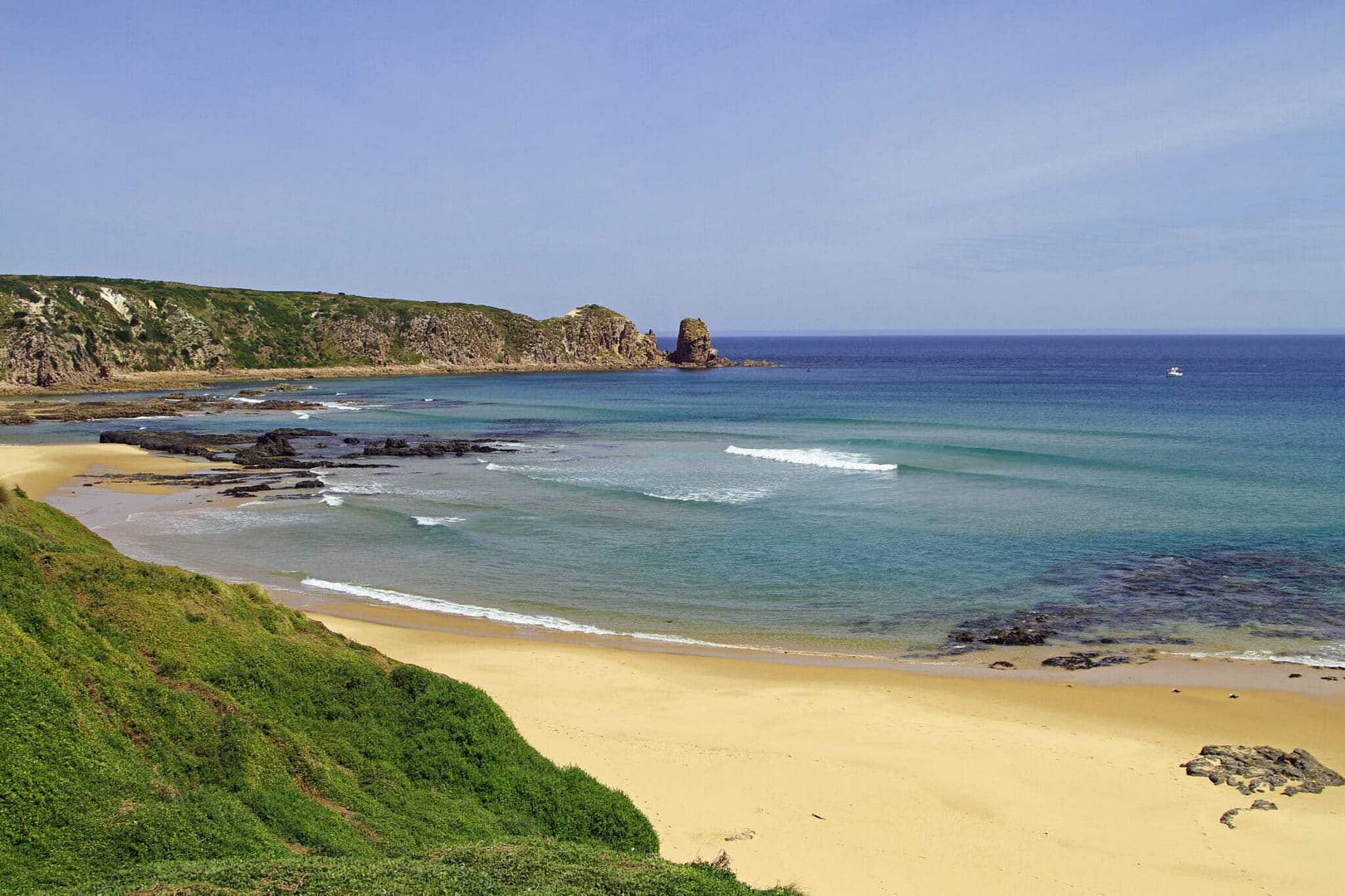 A beach with a rocky shore surrounded by green grass, showcasing the Deluxe Tents and offering an ambiance curated by The Botanist Gin.