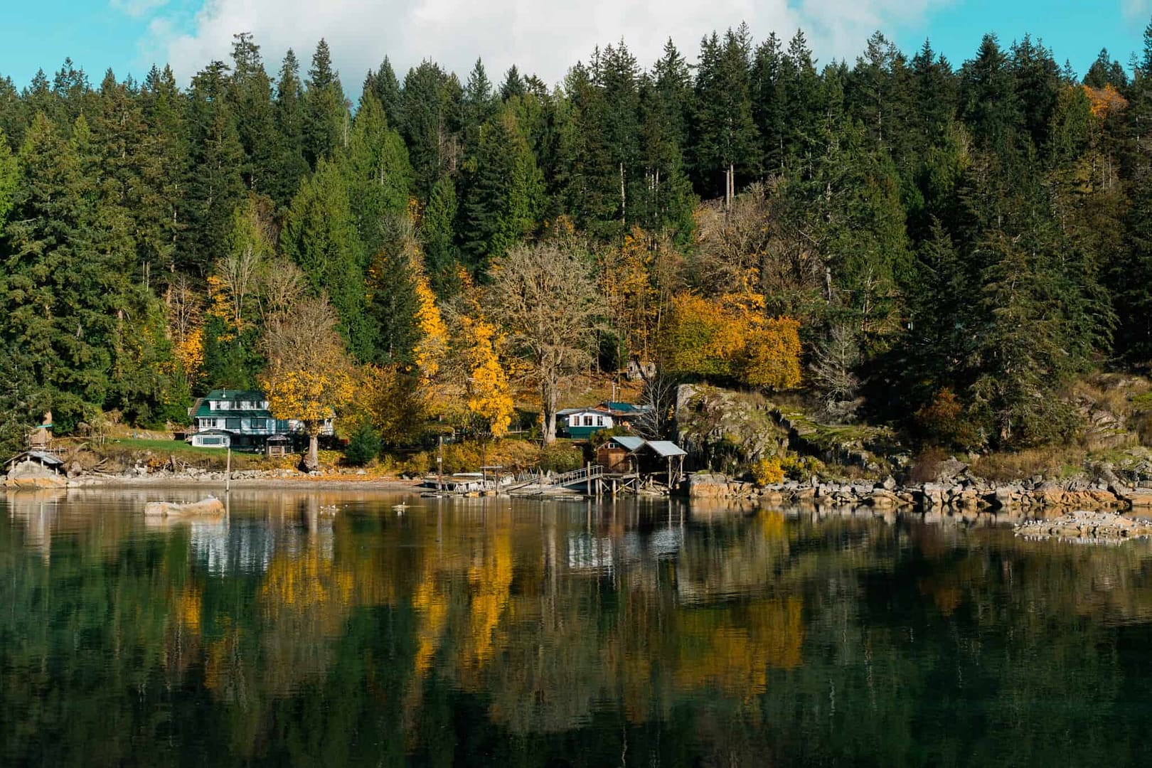 A Land Base house on the shore of a lake surrounded by trees, owned by Klahoose First Nation.