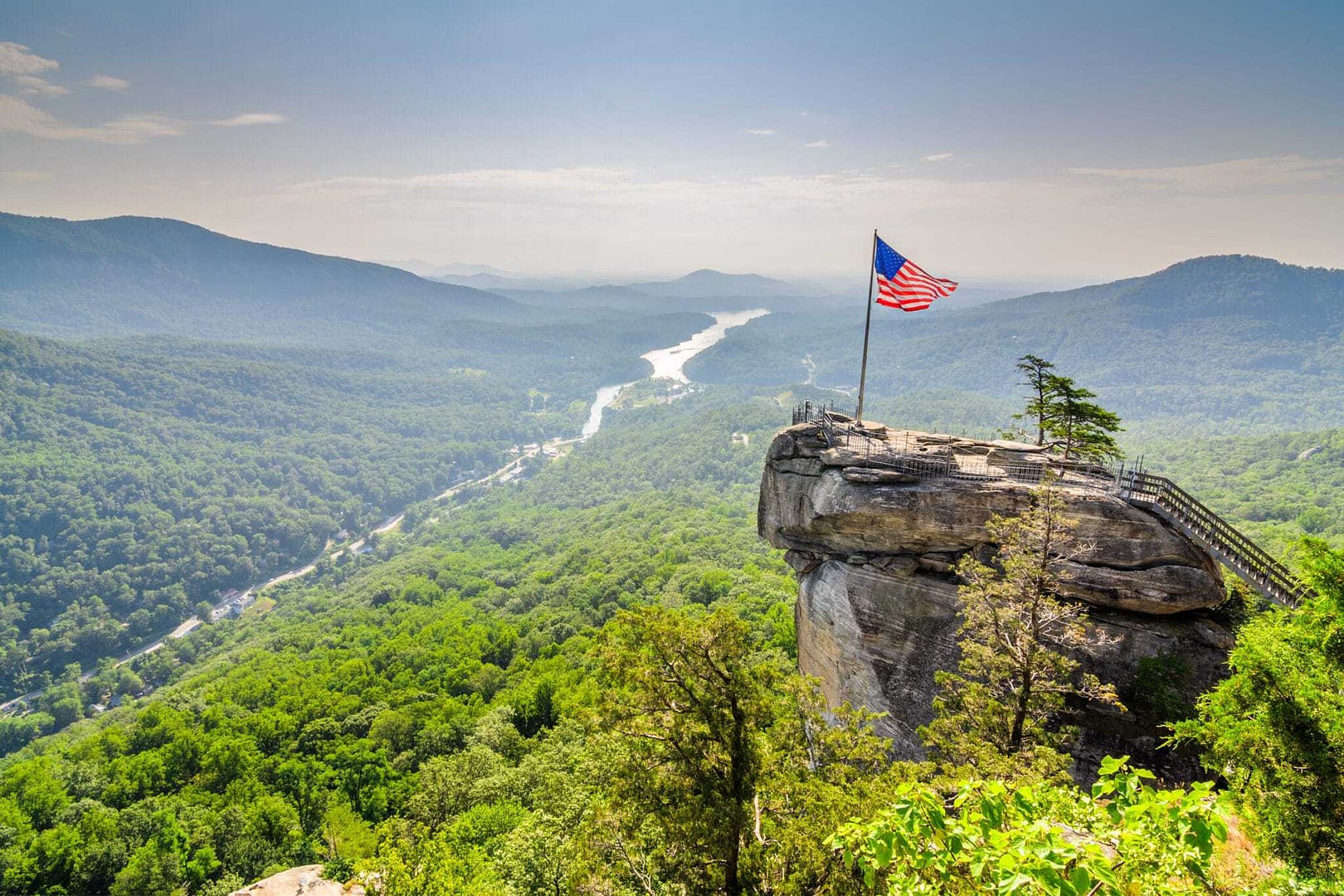 A flag flies on top of a rock overlooking a river in North Carolina, attracting tourists who love to travel.