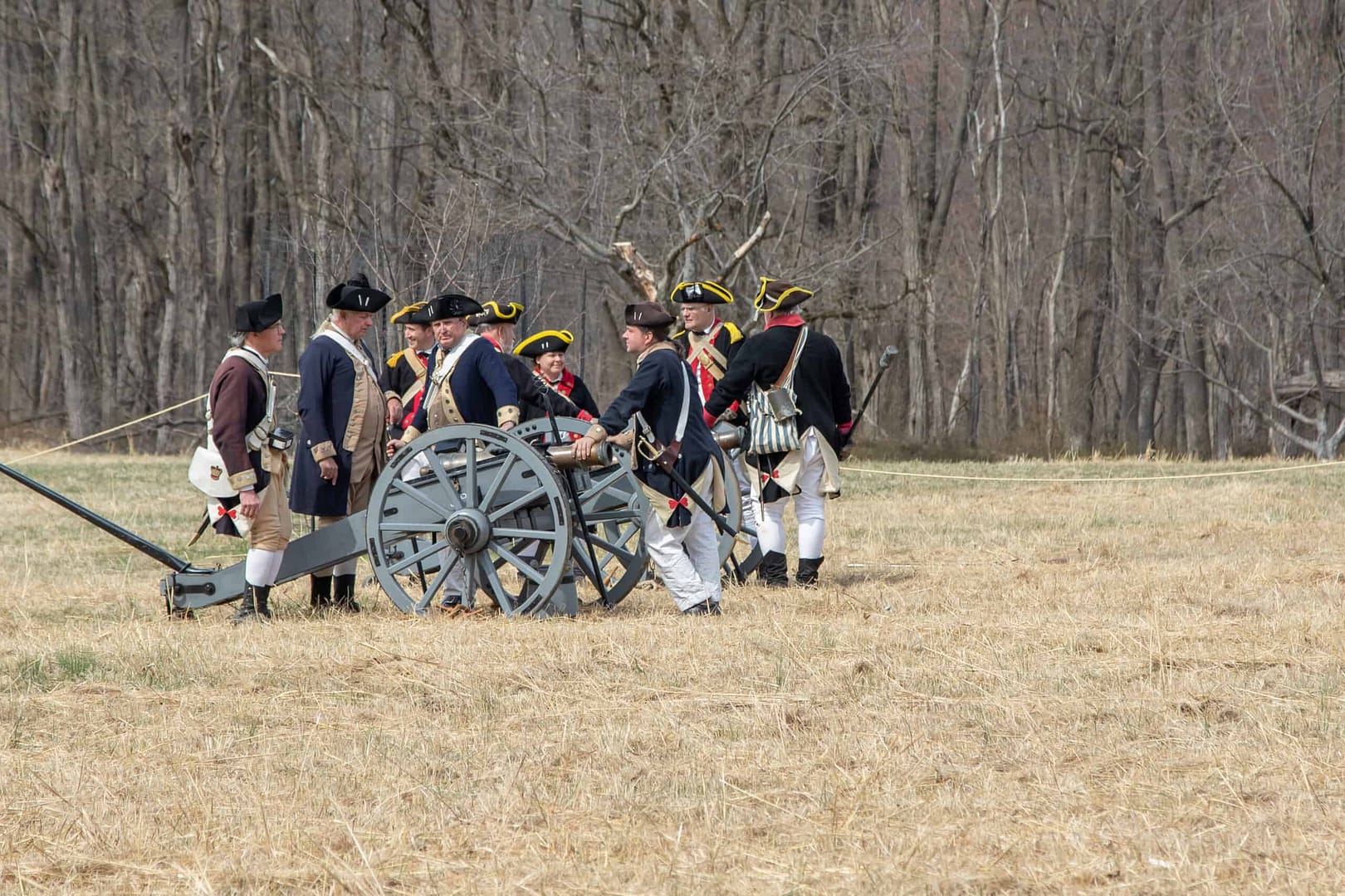 A group of men standing around a Revolutionary War cannon on the battlefield.