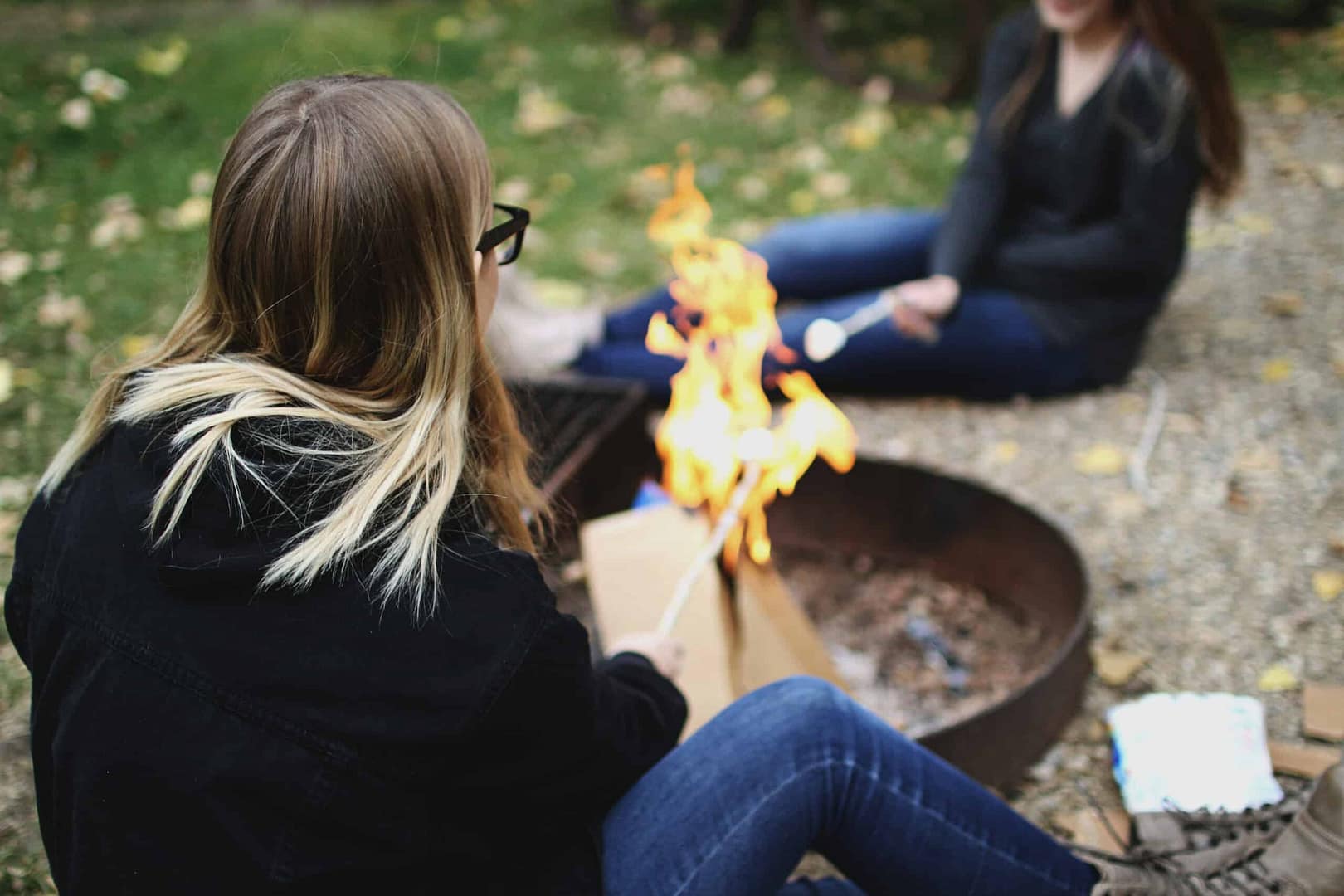 Two girls sitting around a campfire at the Gas City Campground during the summer camping season.