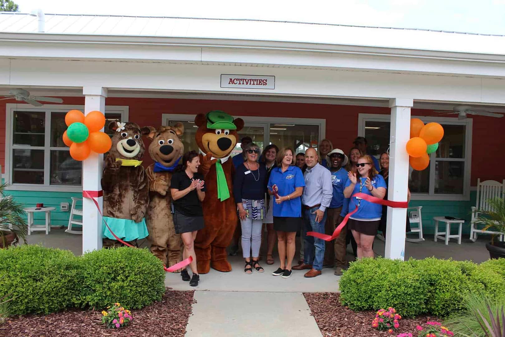 A group of people standing in front of a building at Jellystone Park with bear mascots.