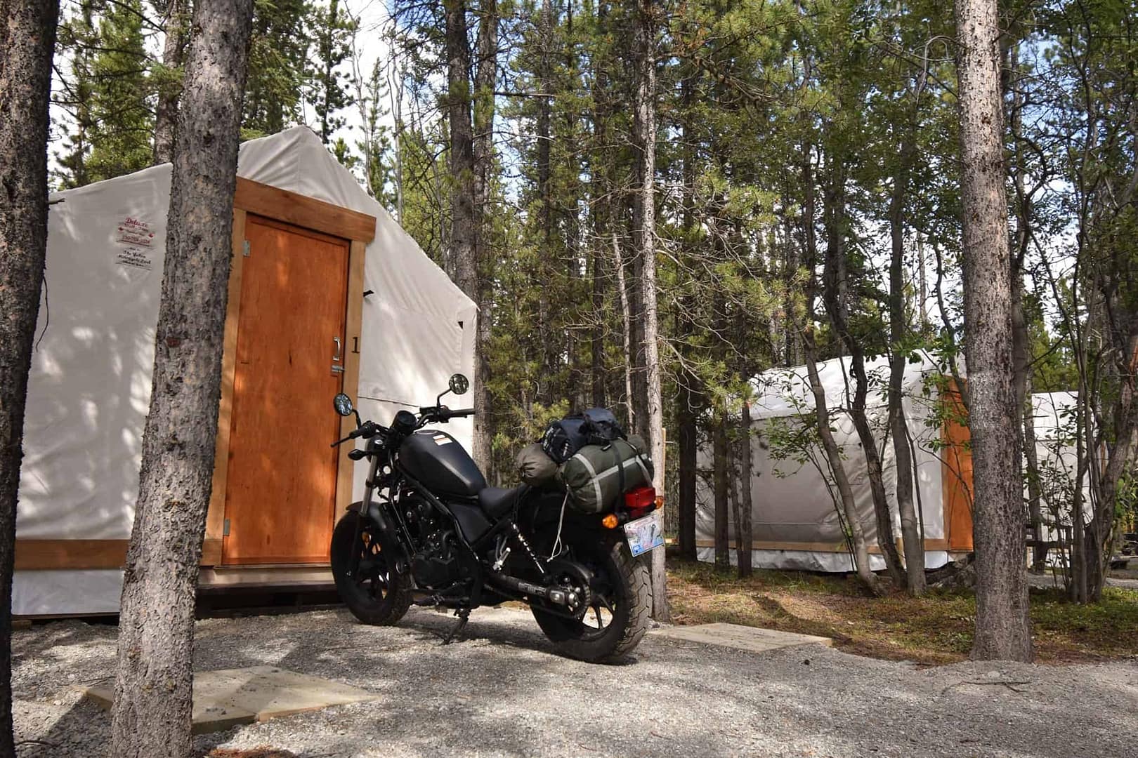 A Yukon motorcycle is parked next to a tent in the woods.