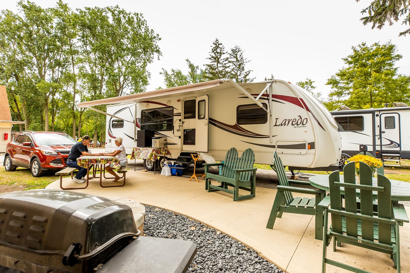 A RV parked in a backyard with a table and chairs near a new splash pad.