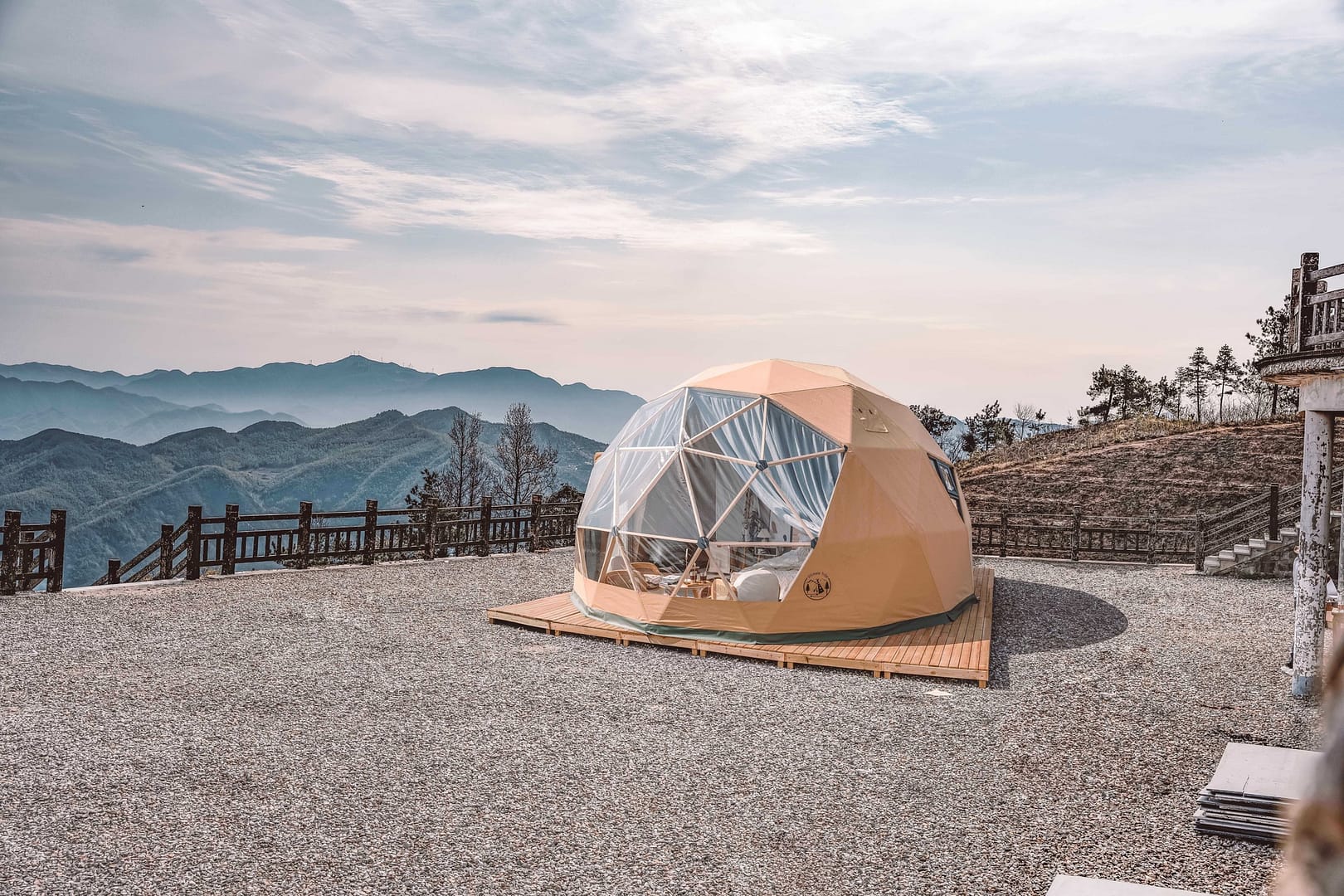 An auto draft geodesic dome tent set on a mountain overlook with panoramic views of distant hills under a clear sky.