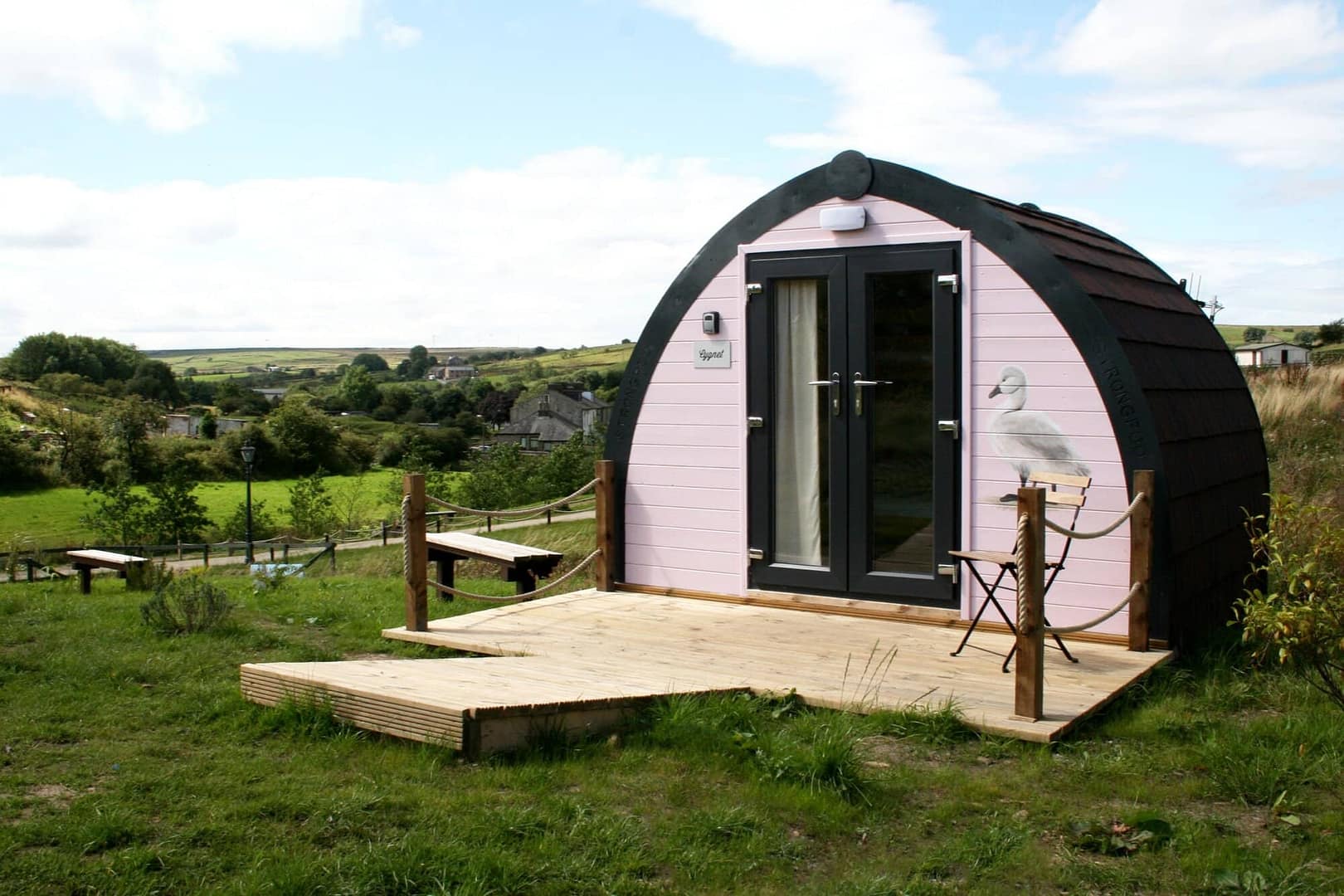 An eco-friendly pod cabin with a wooden deck situated in a rural landscape.