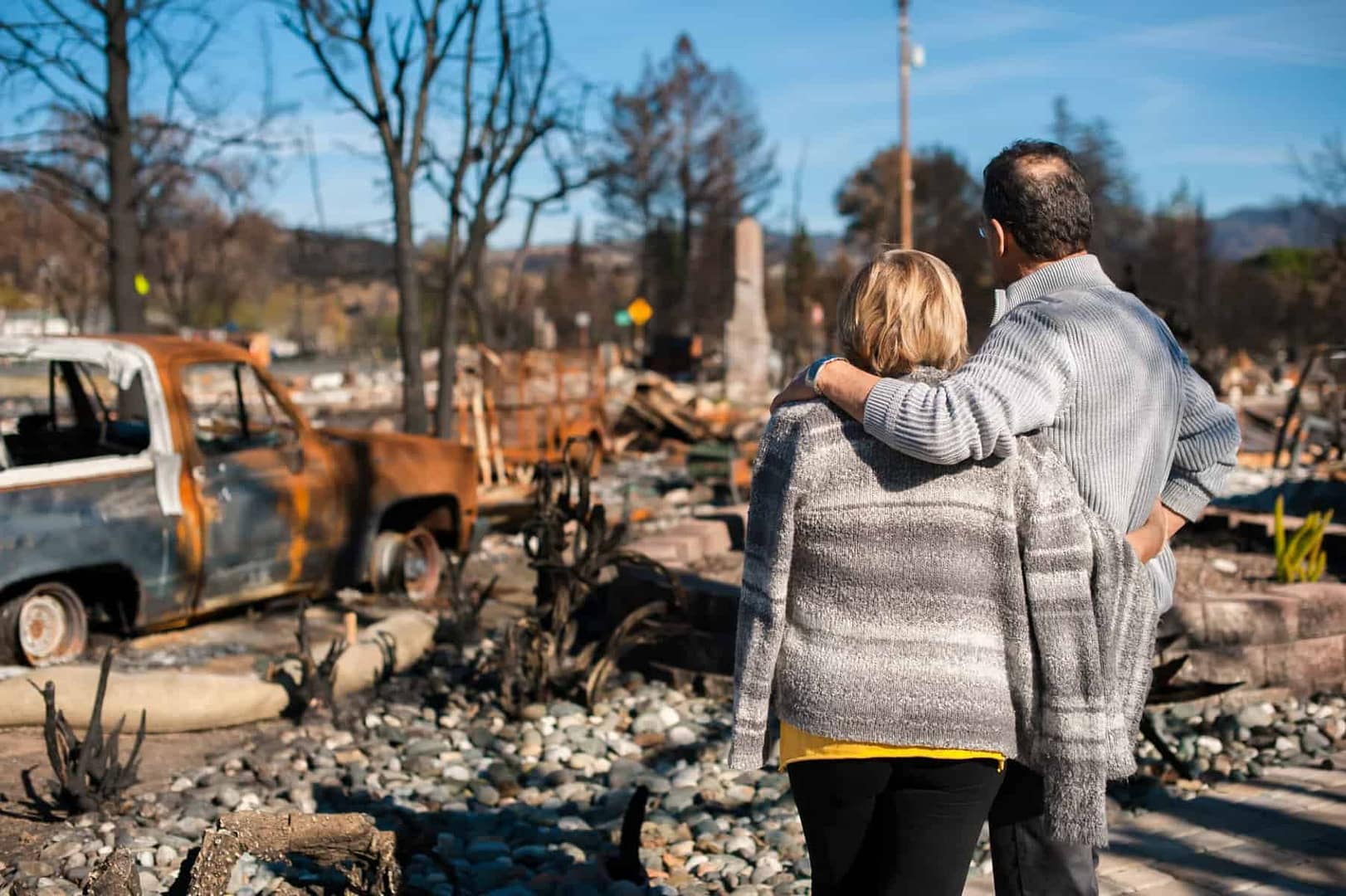 Wildfire evacuees standing in front of a burned out home in British Columbia.