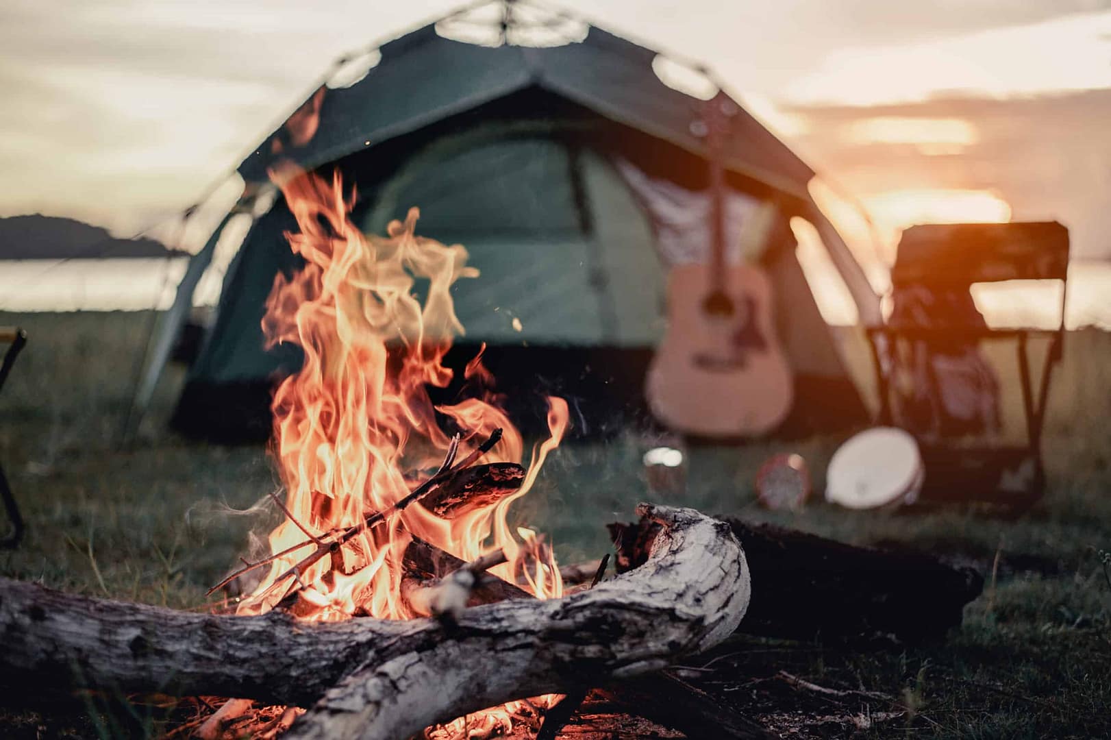 Eurocamp, Europe's leading campsite provider, offers picturesque camping experiences with a cozy campfire in front of a tent and guitar for the enjoyment of campers.