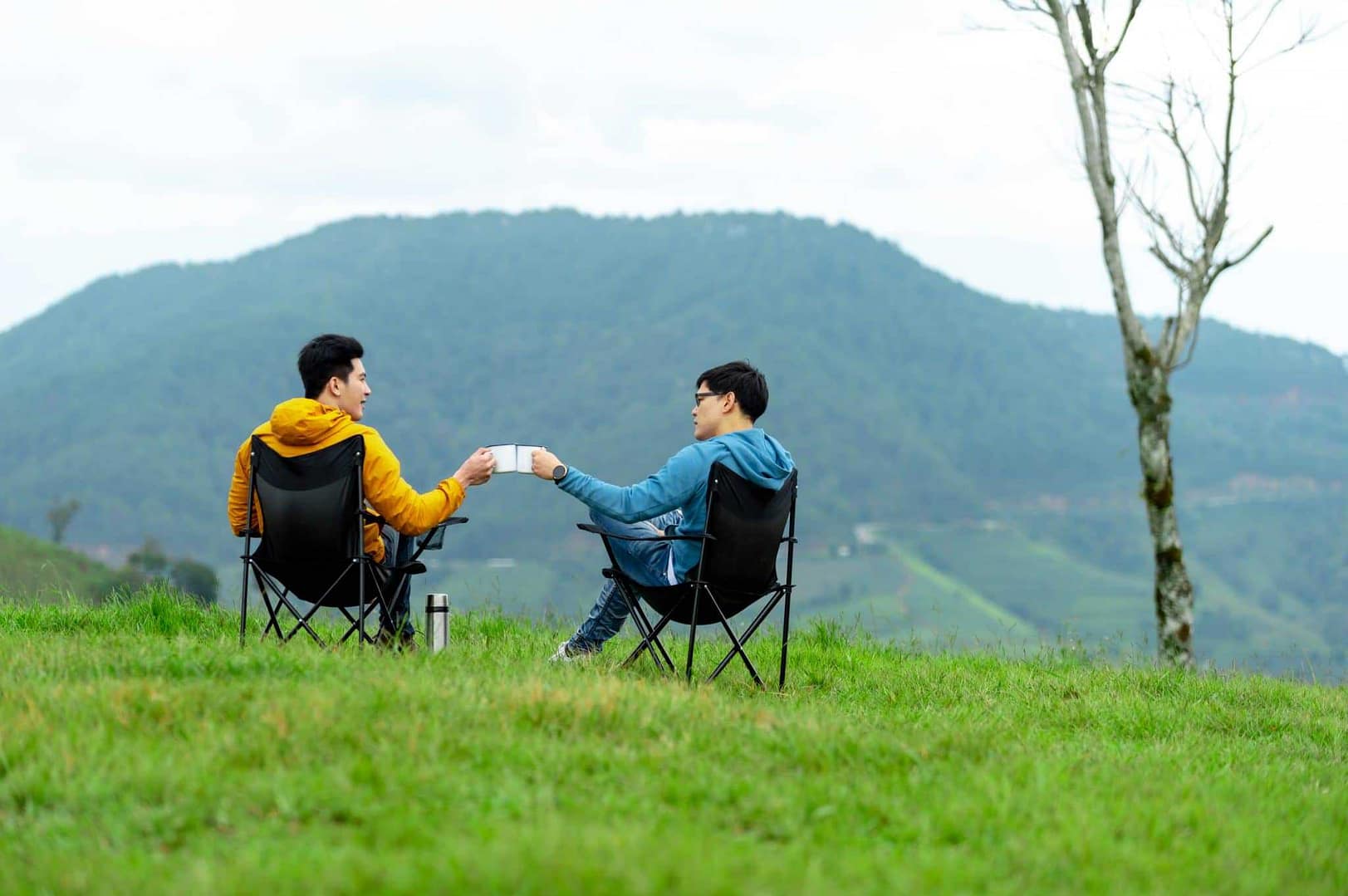 Two people sitting in a folding chair on a grassy hill at an inclusive glamping site near Seoul.